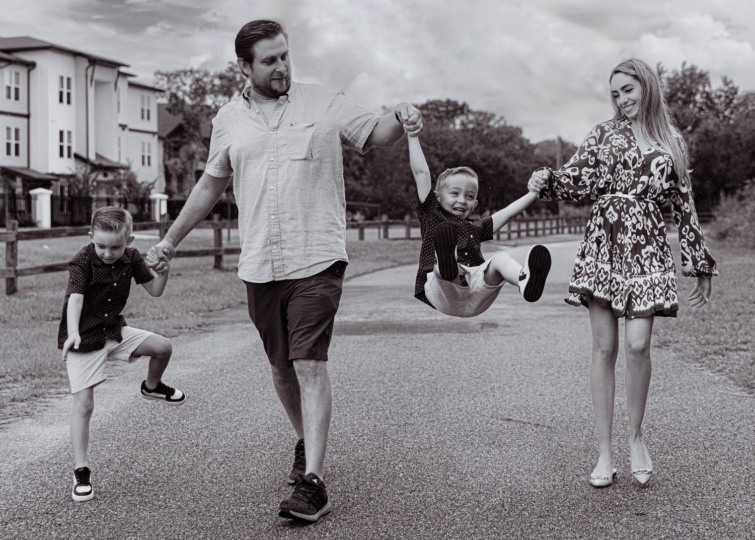 A black and white photo of a family joyfully swinging their child on a suburban street.