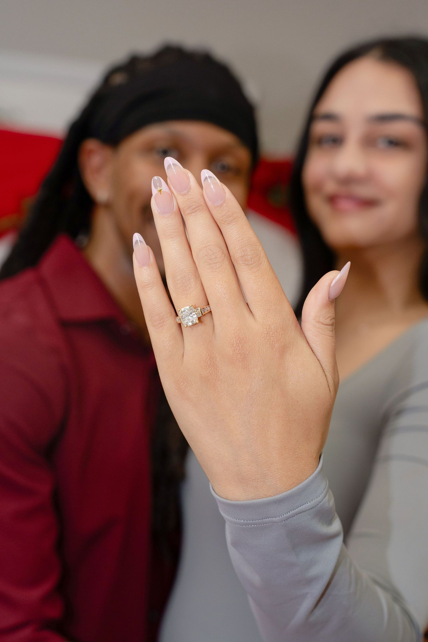 Close-up of engagement ring on woman's hand with couple smiling in background.