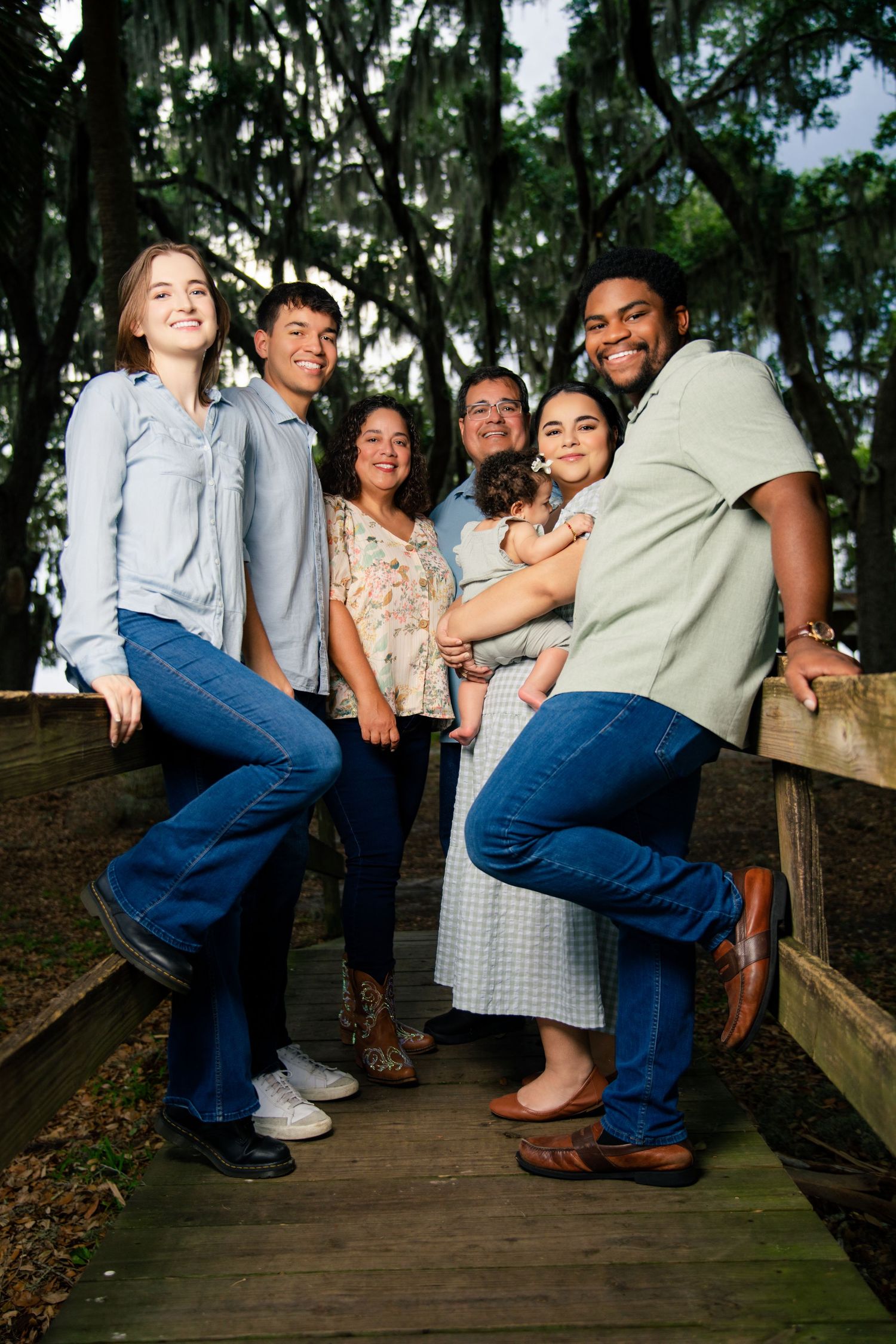 A joyful multigenerational family poses together on a wooden bridge surrounded by moss-covered trees.