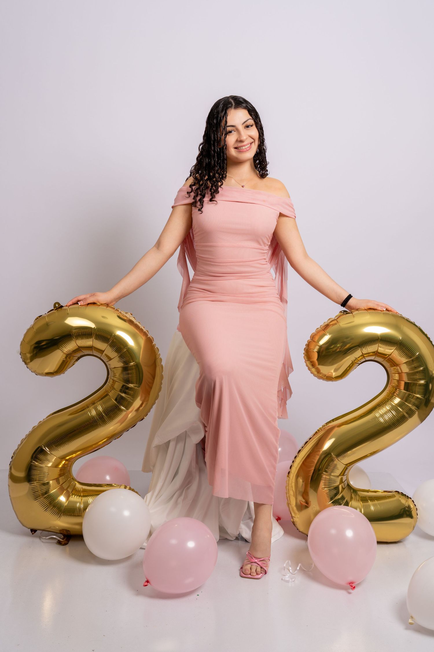 A smiling woman in a pink dress poses between two large gold number 22 balloons.