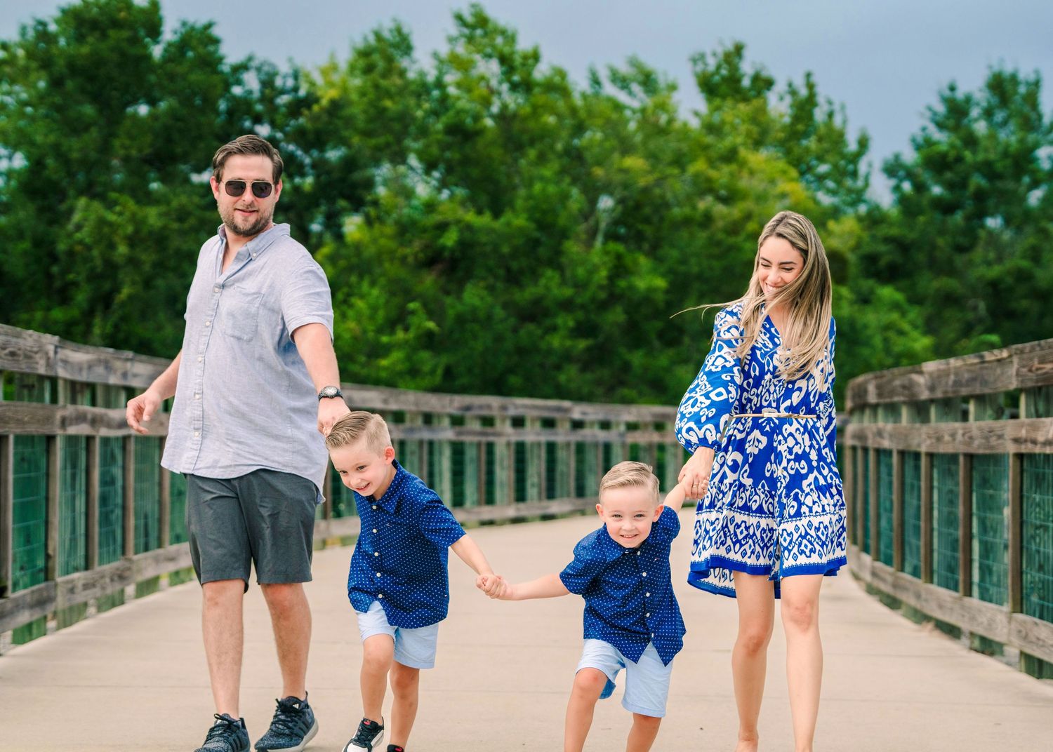 Happy family with two young boys walking on a wooden bridge outdoors.