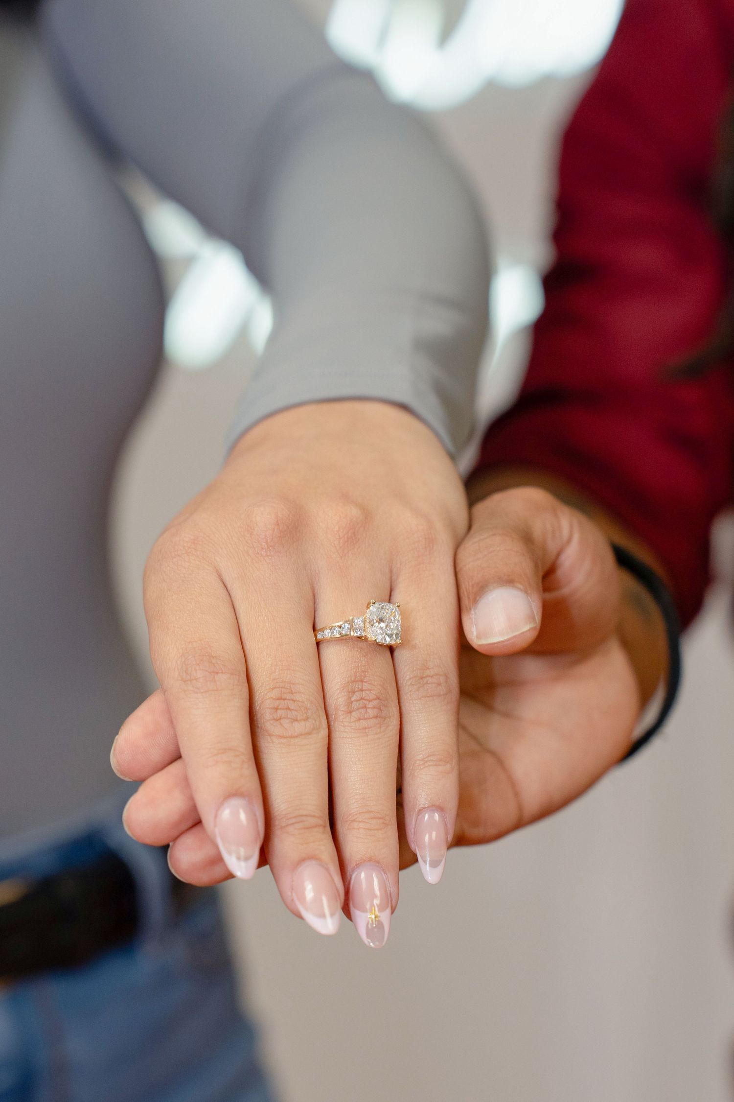 Close-up of woman's hand displaying diamond engagement ring while resting on partner's hand.