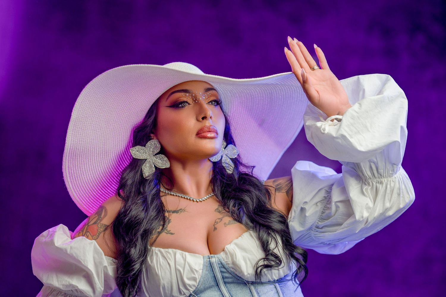 Woman performing on stage wearing a white wide-brim hat and butterfly earrings under purple lights.