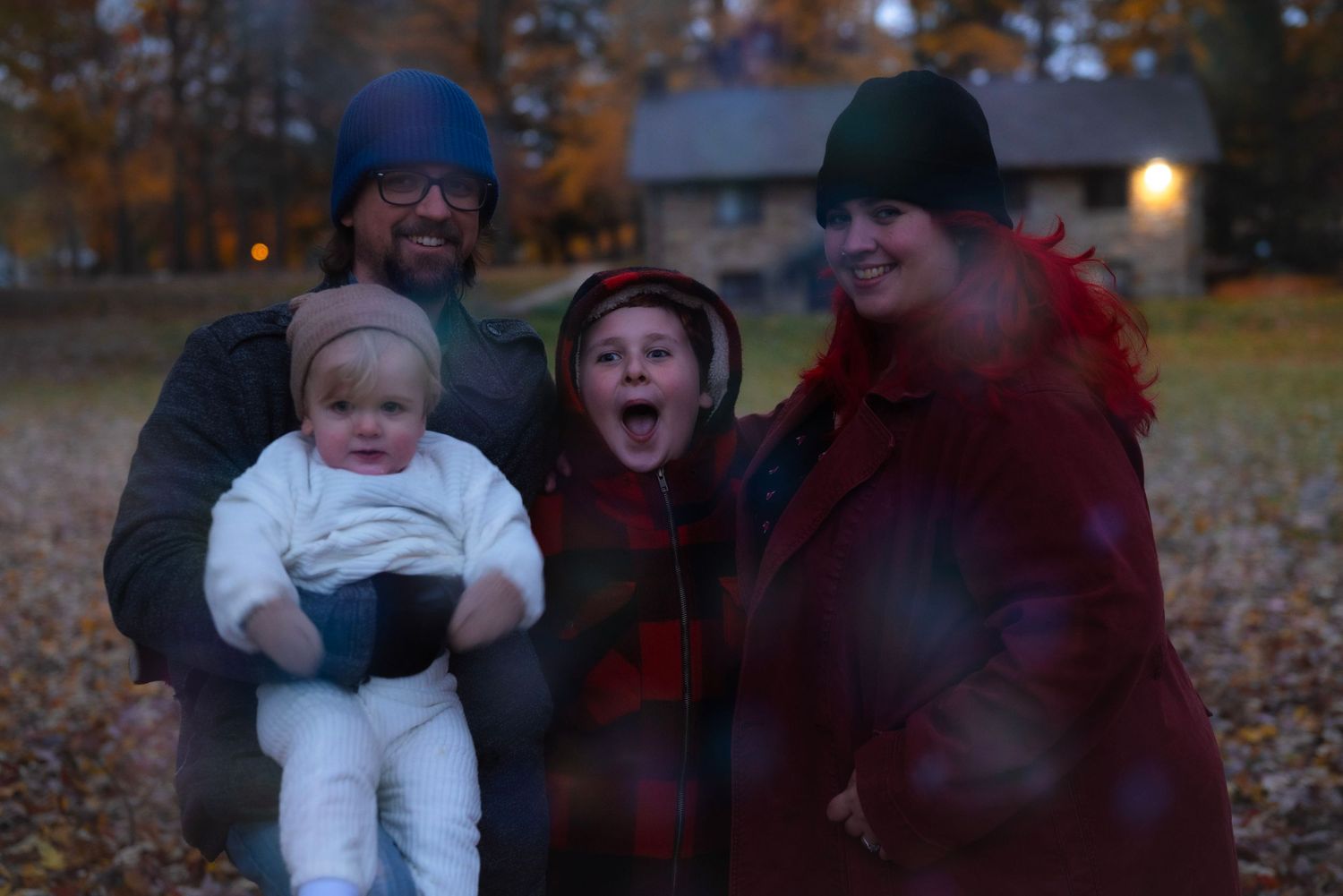 Family of four posing outdoors among autumn leaves at dusk. Neo Ohio, outdoors, family.