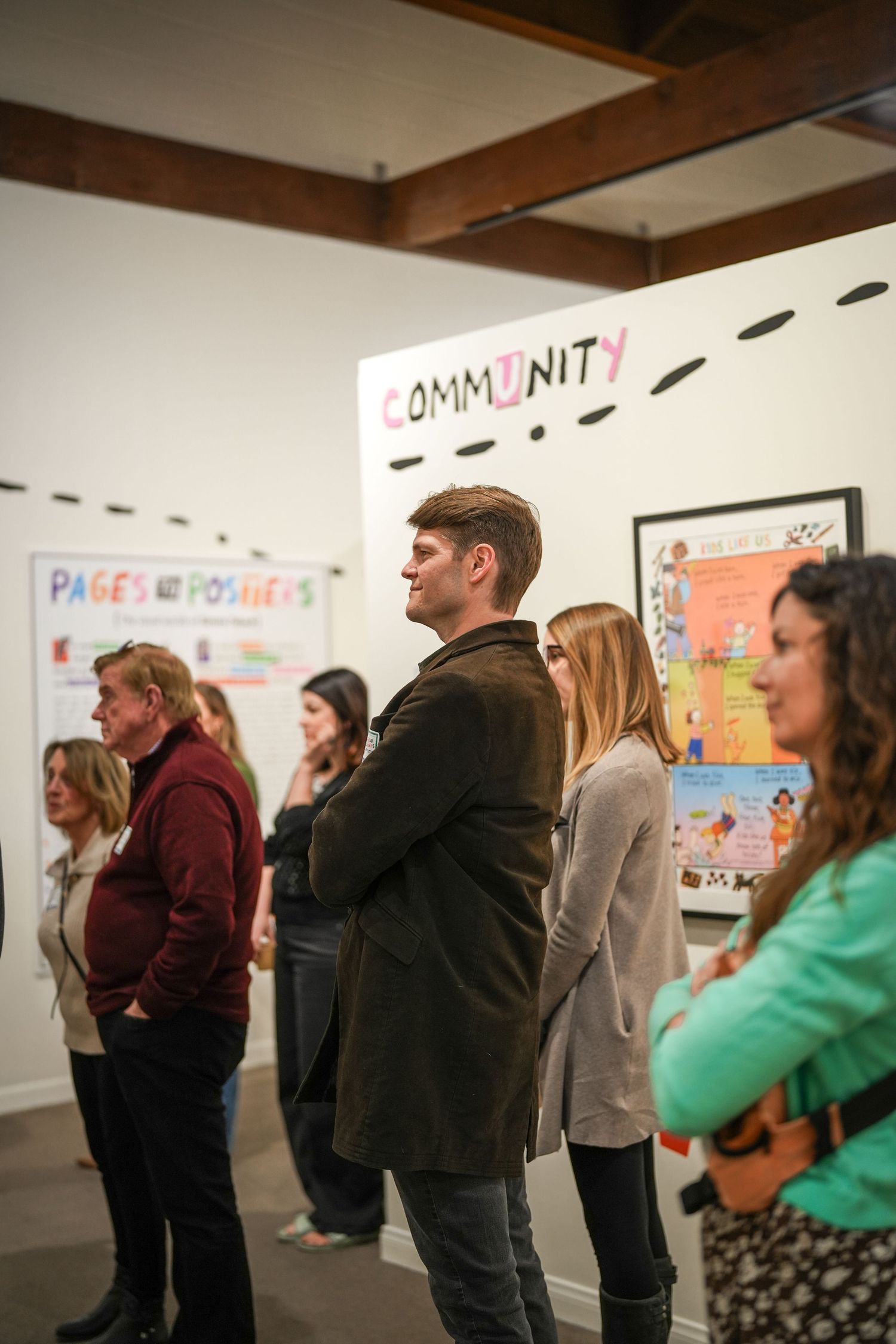 Gallery visitors stand and look at wall displays under a Community sign at an art exhibition opening.