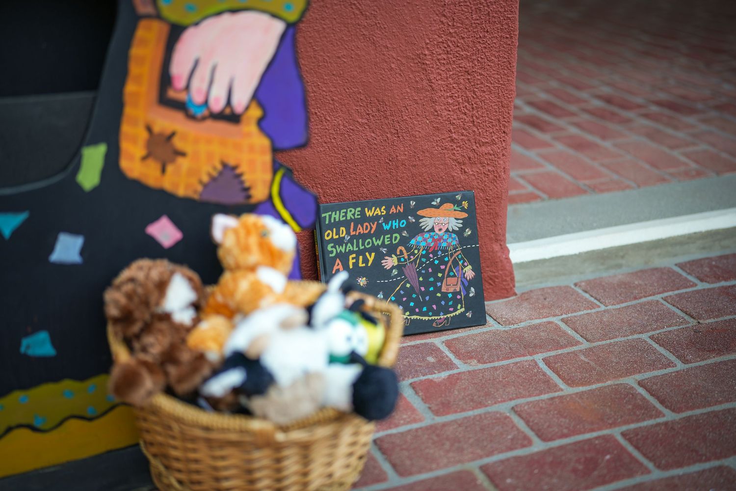 Wicker basket of plush toy animals beside a colorful display and a chalkboard sign referencing the old lady who swallowed a fly.