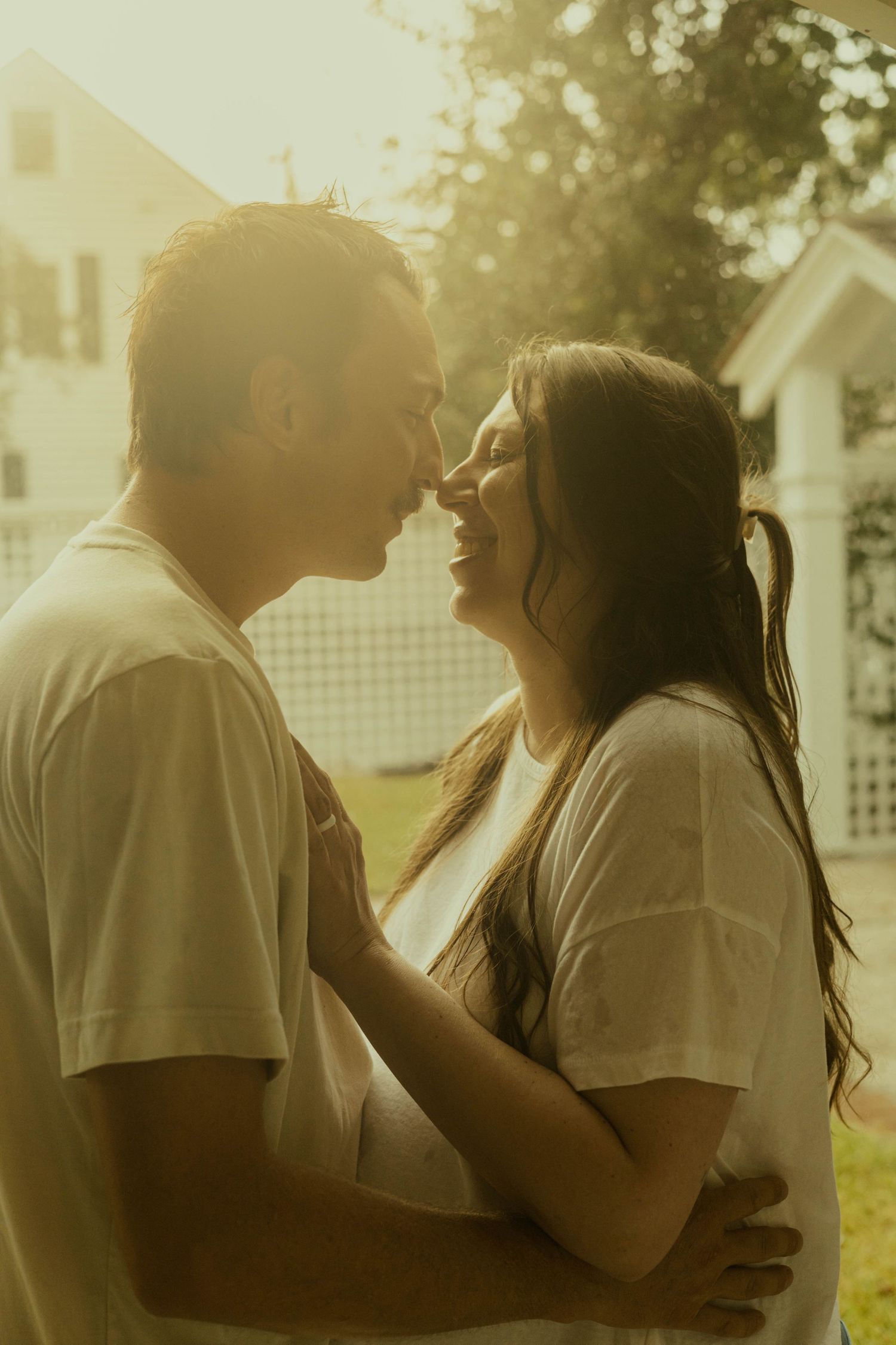 Expecting couple share a joyful nose-to-nose moment outdoors in warm golden light during a romantic maternity photoshoot.