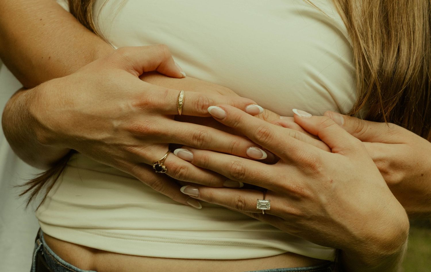 Close-up of a couple's intertwined hands showing engagement and wedding rings in a warm embrace.