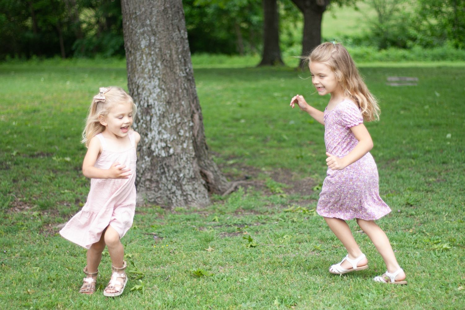 Vibrant outdoor family photography of two young girls running and playing together on a sunlit path at Chisholm Trail Park in Plano, Texas.