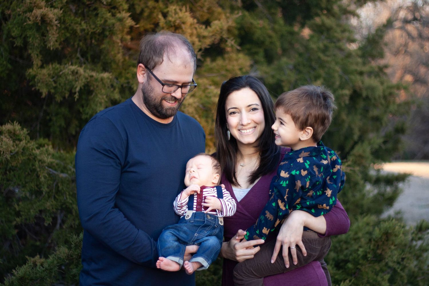 Family photography featuring parents with their toddler son and newborn baby during a sunlit outdoor photo shoot at Chisholm Trail.