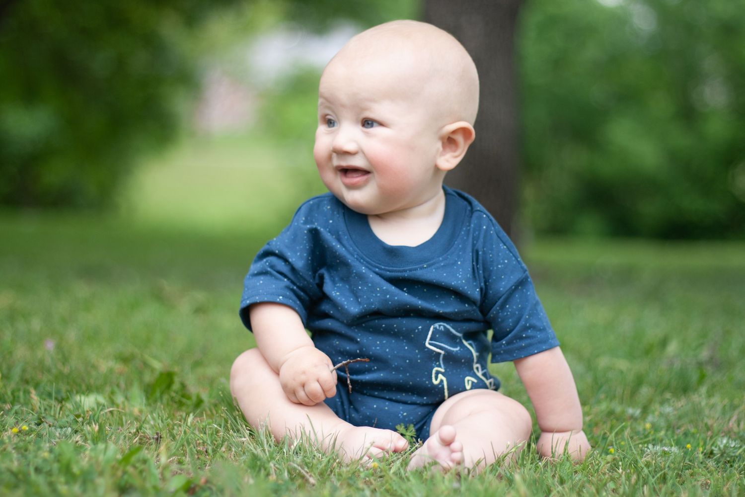 Vibrant outdoor baby photography of a smiling baby boy sitting in the grass during a family session at Chisholm Trail Park in Plano.