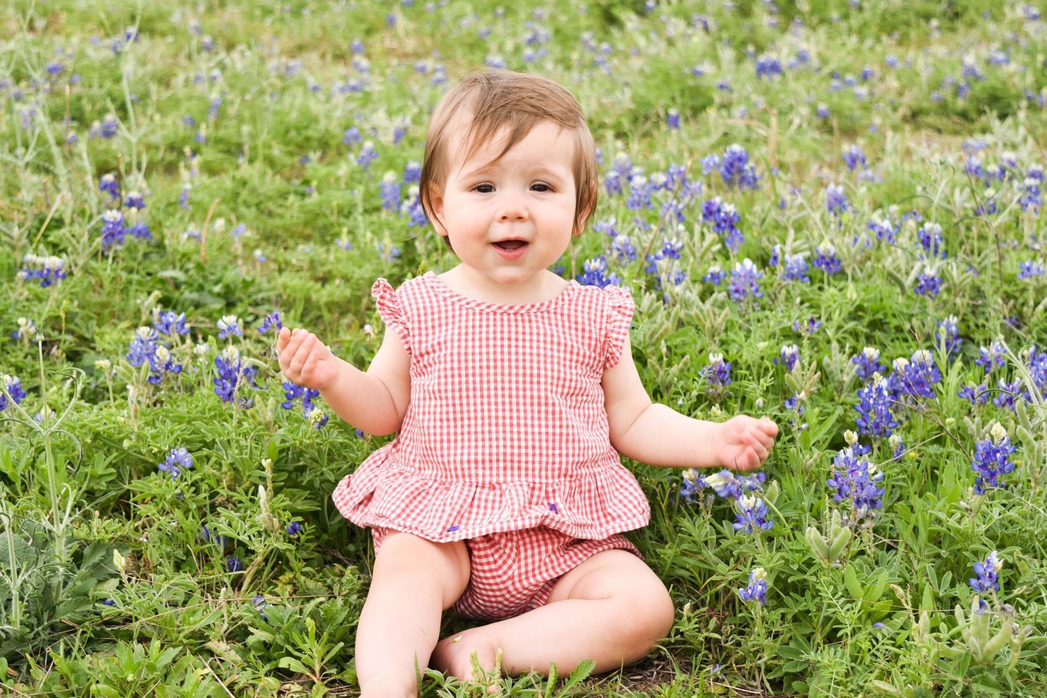 True-to-life portrait of a baby girl smiling in a beautiful field of Texas bluebonnets during an outdoor milestone photo shoot in Plano.