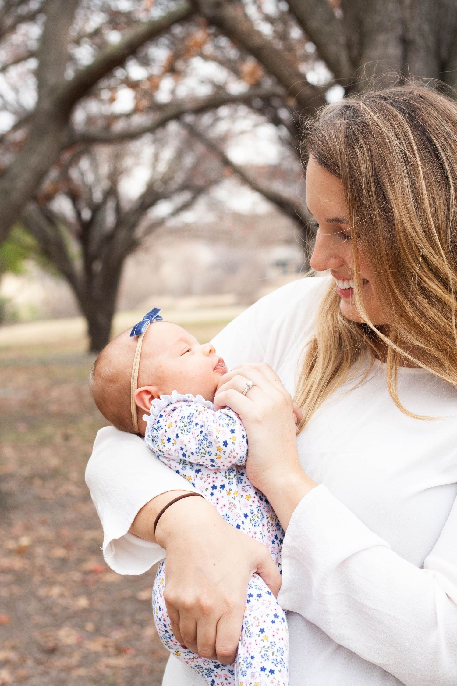 Vibrant outdoor family photography of a happy mother holding her newborn baby and smiling during a sunlit portrait session in North Dallas.