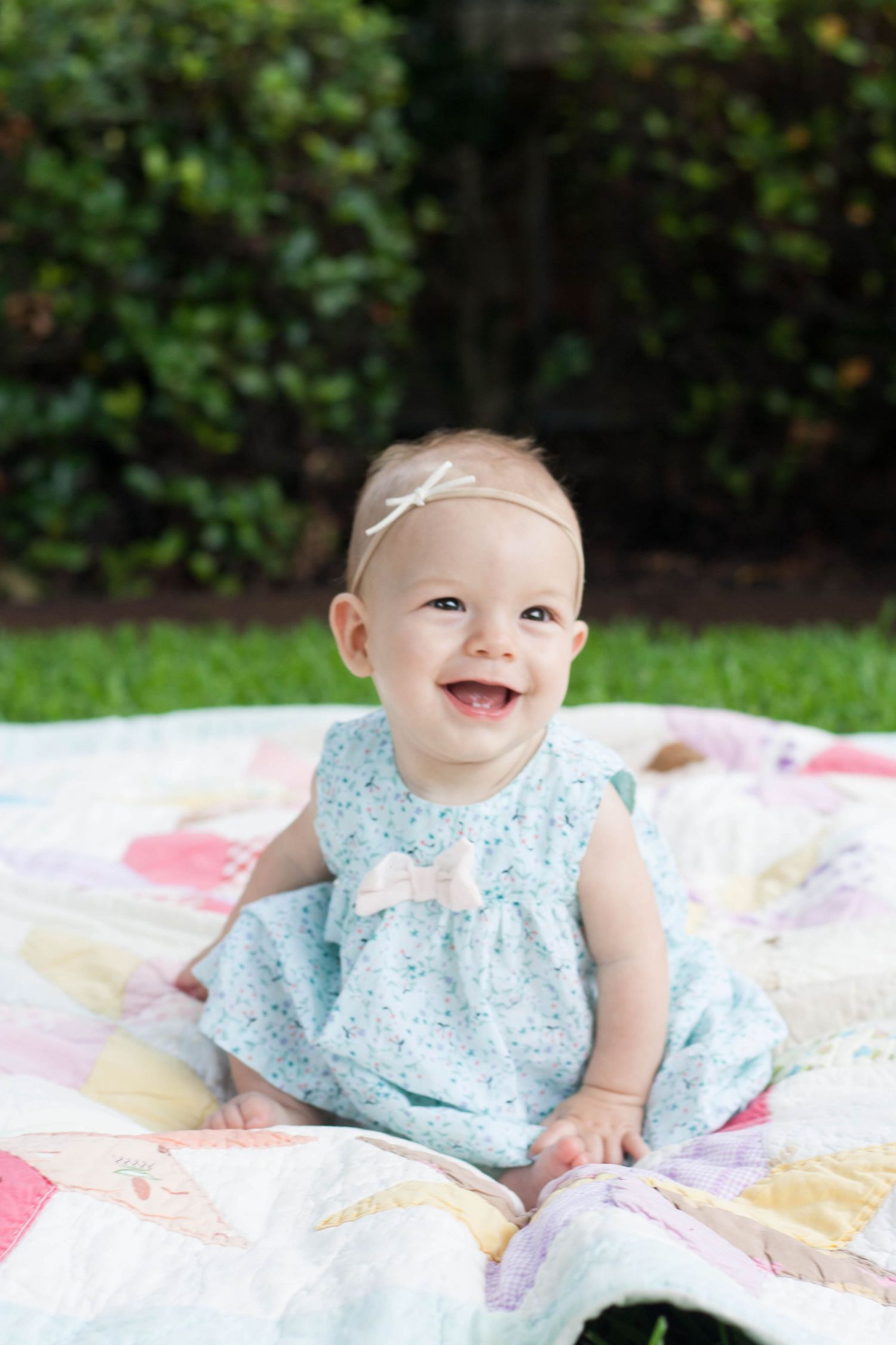 Vibrant outdoor baby photography of a smiling baby girl sitting in the grass during a family session at Chisholm Trail Park in Plano, TX.