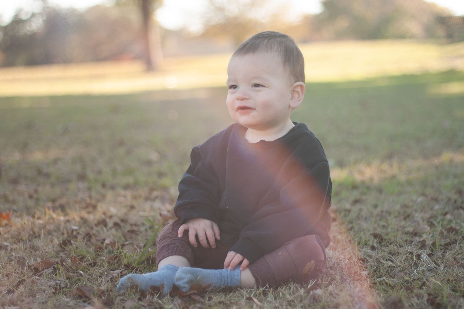 Vibrant outdoor baby photography of a smiling baby boy against a beautifully blurred, sunlit background at Horseshoe Park in Plano, Texas.