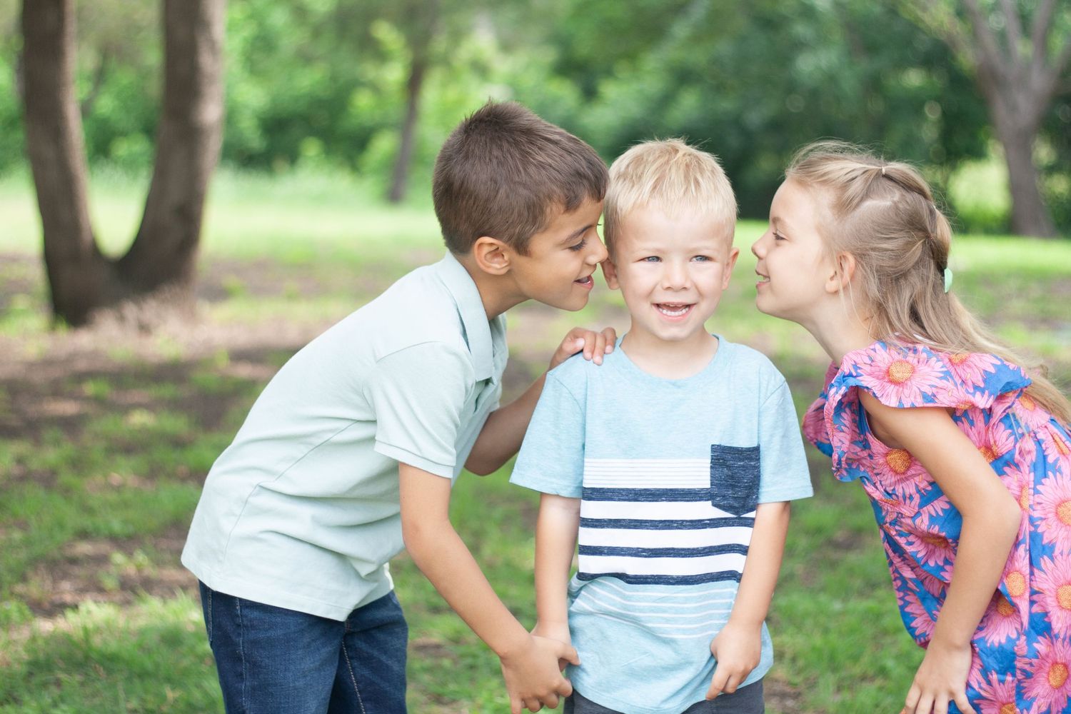 Outdoor sibling photography of an older brother and sister kissing their younger sibling on the cheeks at Chisholm Trail Park in Plano.