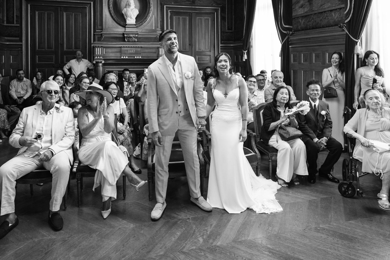 La mariée et le mari se tiennent debout, souriants et riant, lors d'une cérémonie dans une salle ornée de panneaux