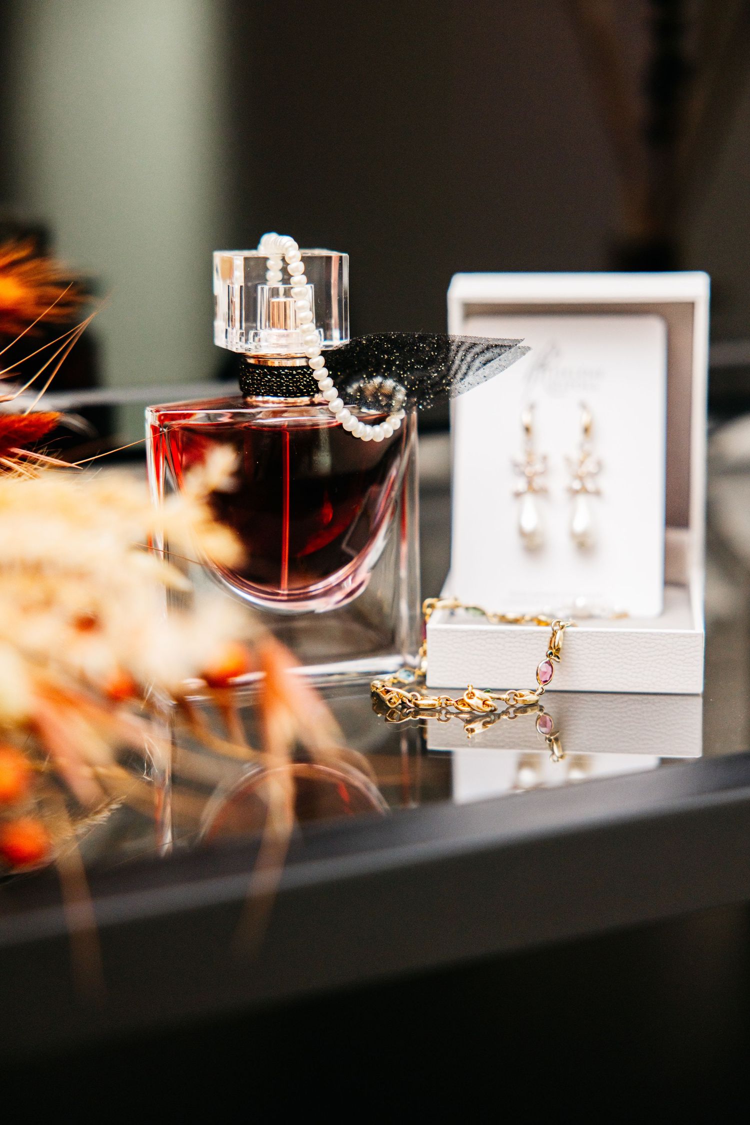 Perfume bottle with pearl necklace, gold bracelet and pearl drop earrings in a gift box, displayed as wedding day accessories.