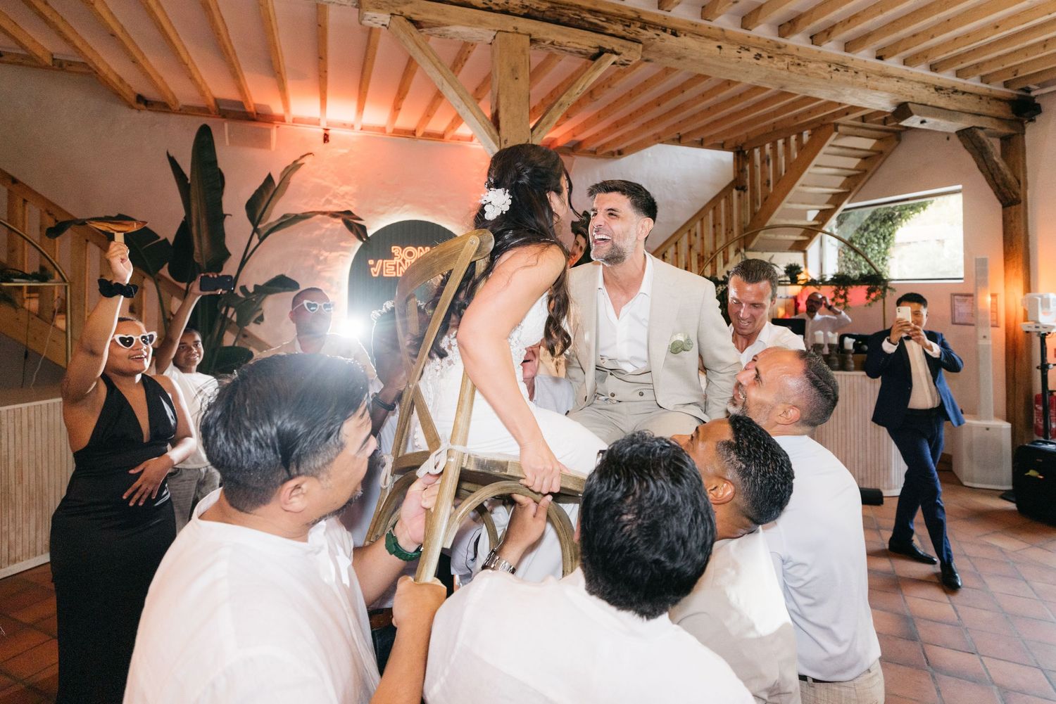 Les invités soulèvent la mariée et le marié sur des chaises lors d'une danse traditionnelle joyeuse lors d'une réception de mariage rustique