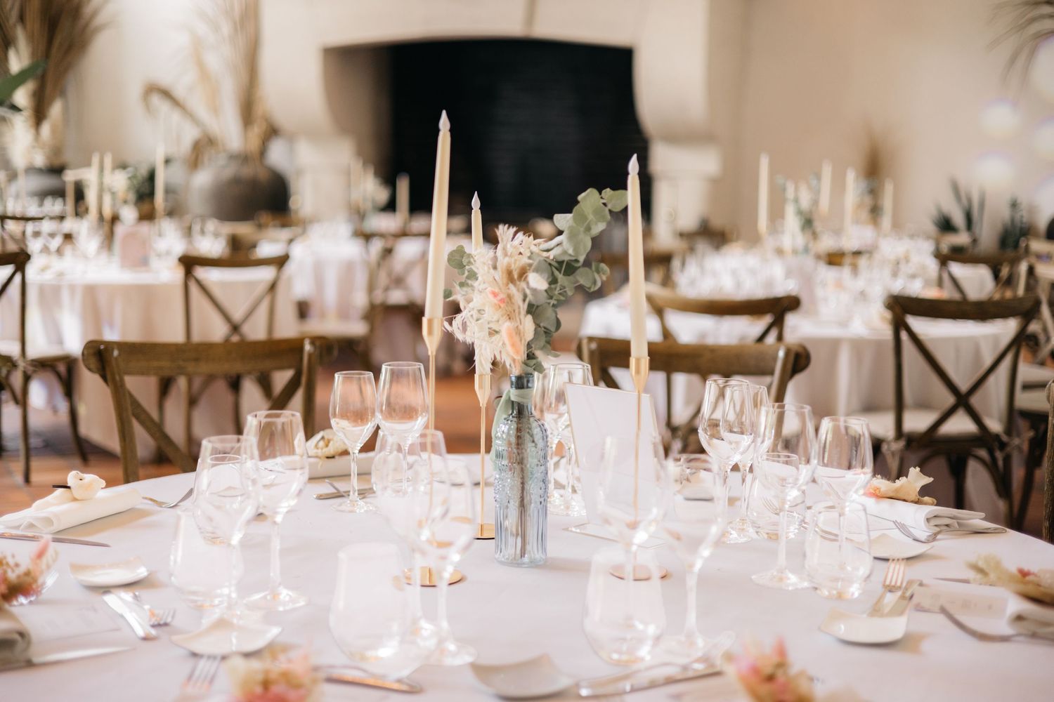 Table élégante de réception de mariage avec du verre, de longues bougies et un centre de table floral doux dans un lieu rustique lumineux.