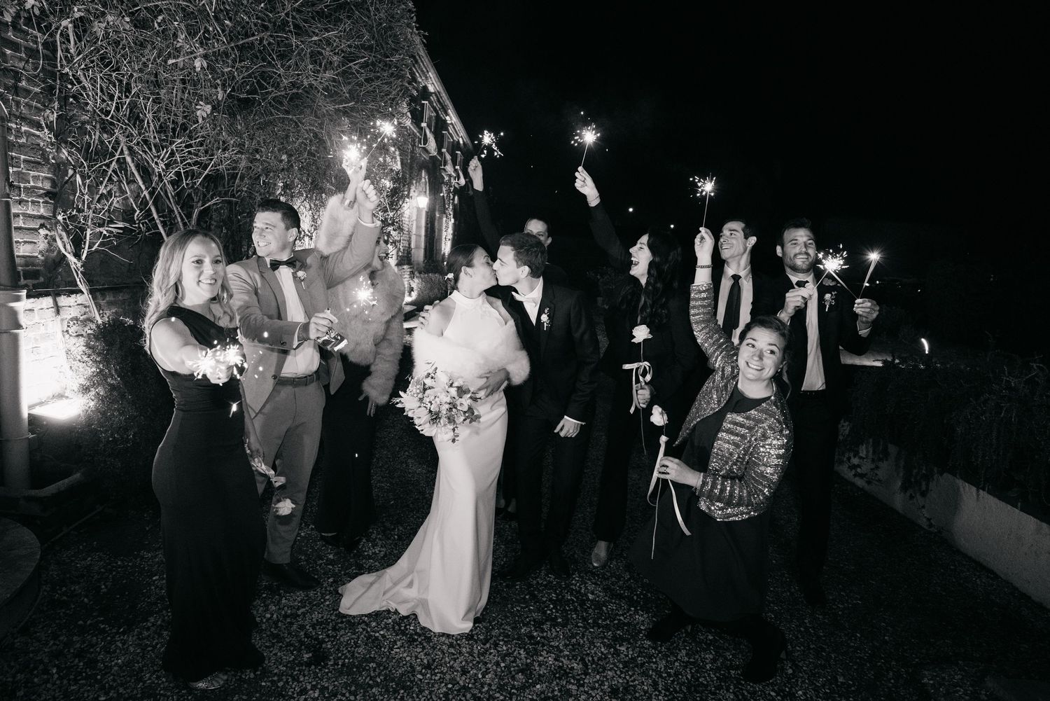 La mariée et ses invités célèbrent le mariage dehors, à la lueur des lumières, en noir et blanc.