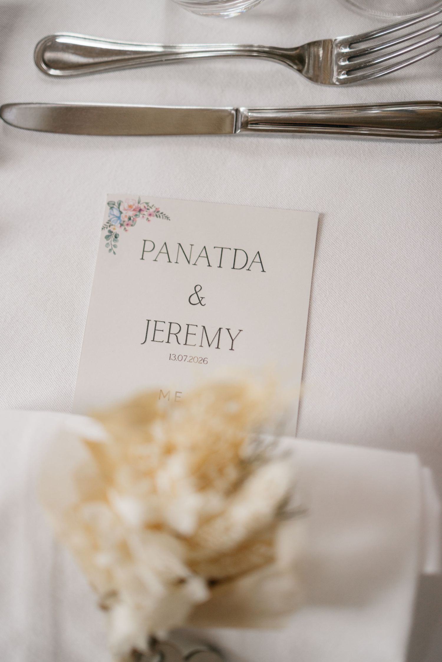 Personalized wedding menu card for Panatda and Jeremy resting on a white napkin with dried flower decoration and silverware.