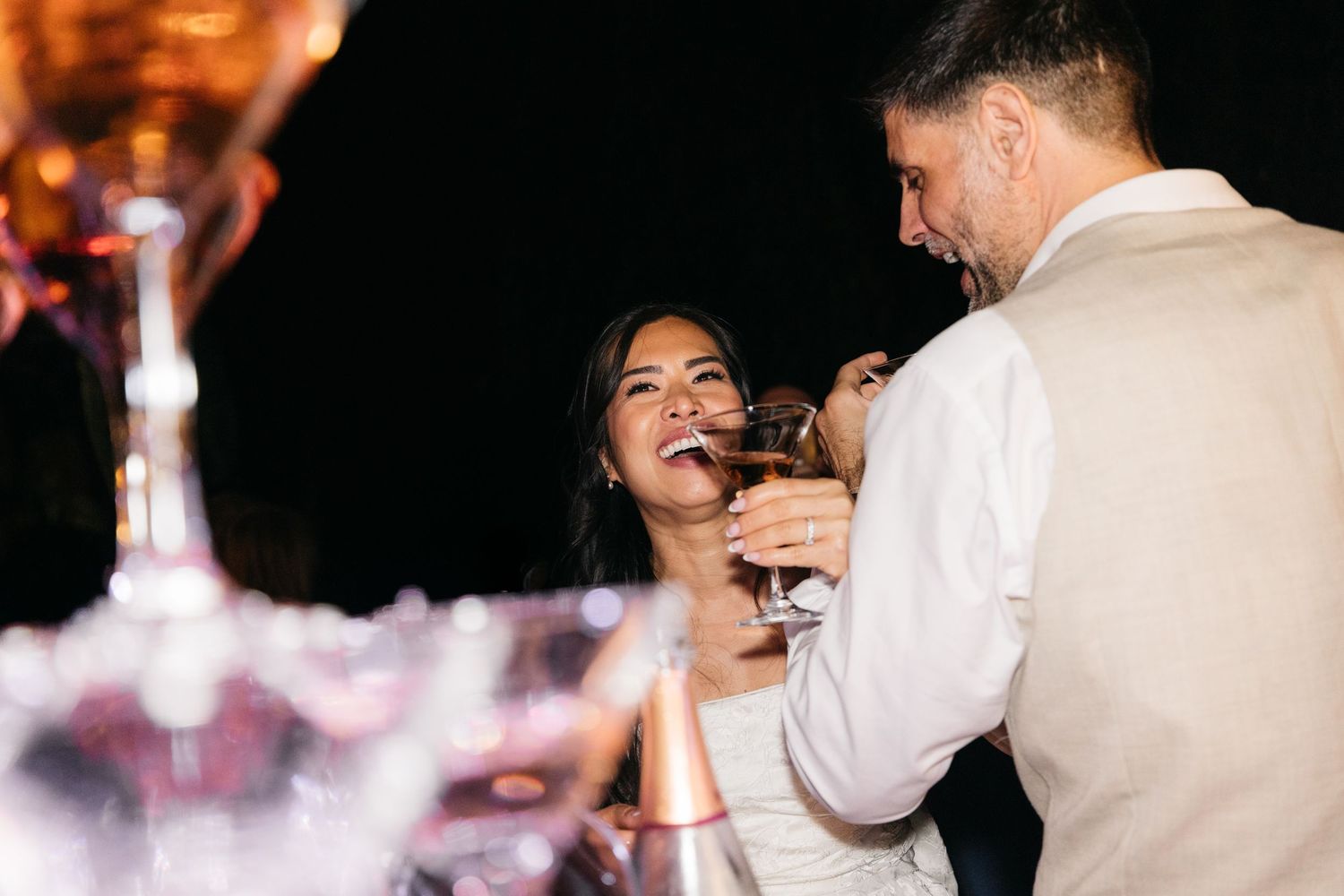 Bride and groom share a joyful moment toasting with champagne glasses beside a sparkling champagne tower at their wedding.