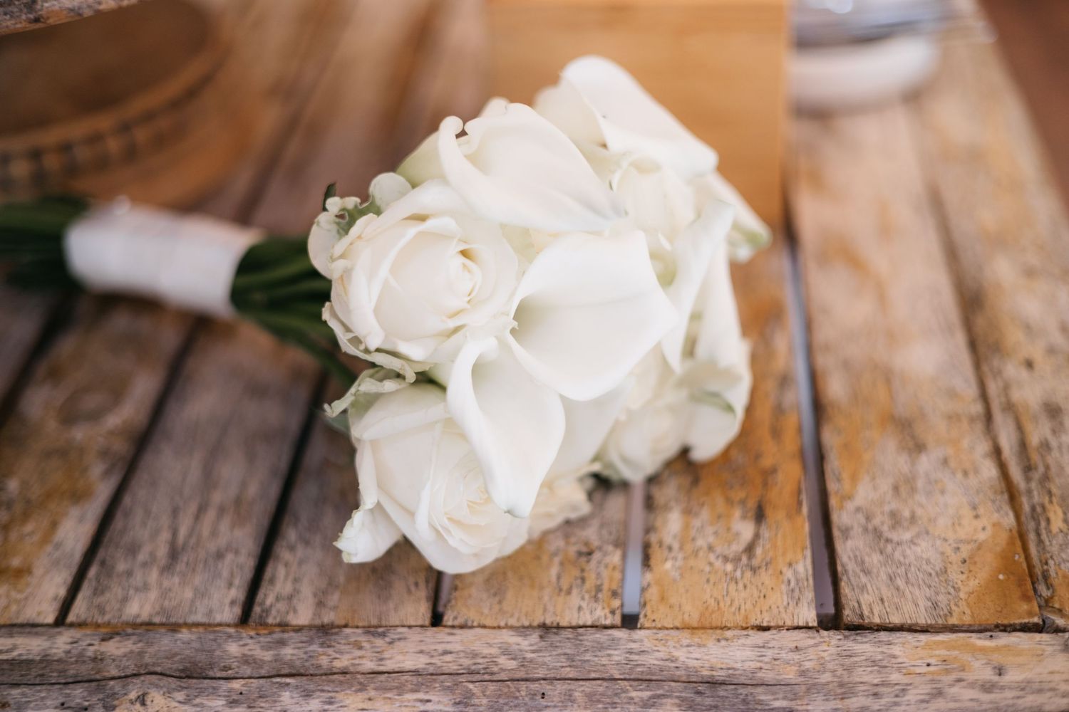 Bouton d'oraisons de roses blanches enveloppées dans un ruban blanc reposant sur une surface en bois rustique usée.