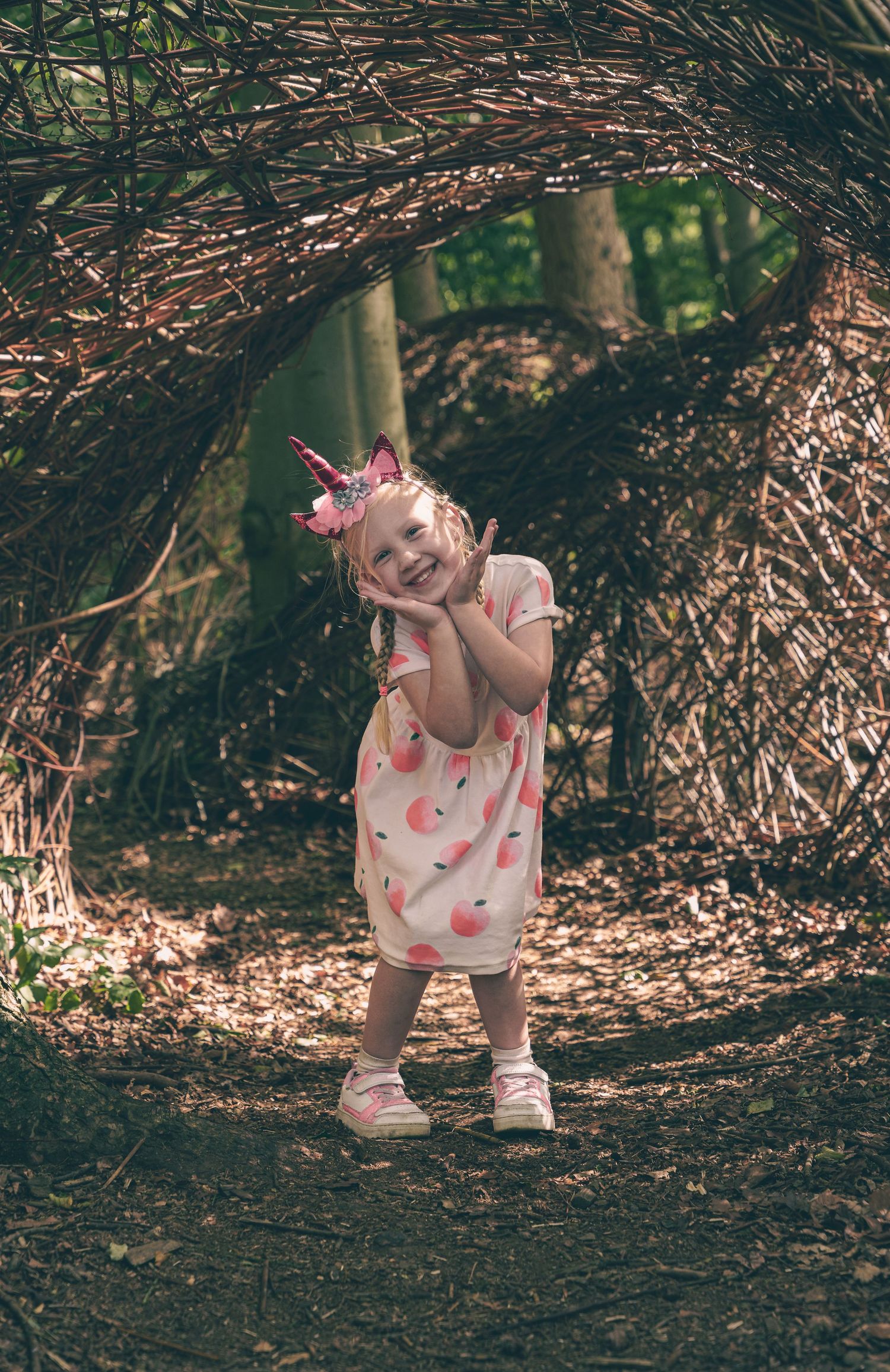 Small child exploring a natural tunnel made of branches while wearing a polka dot dress.