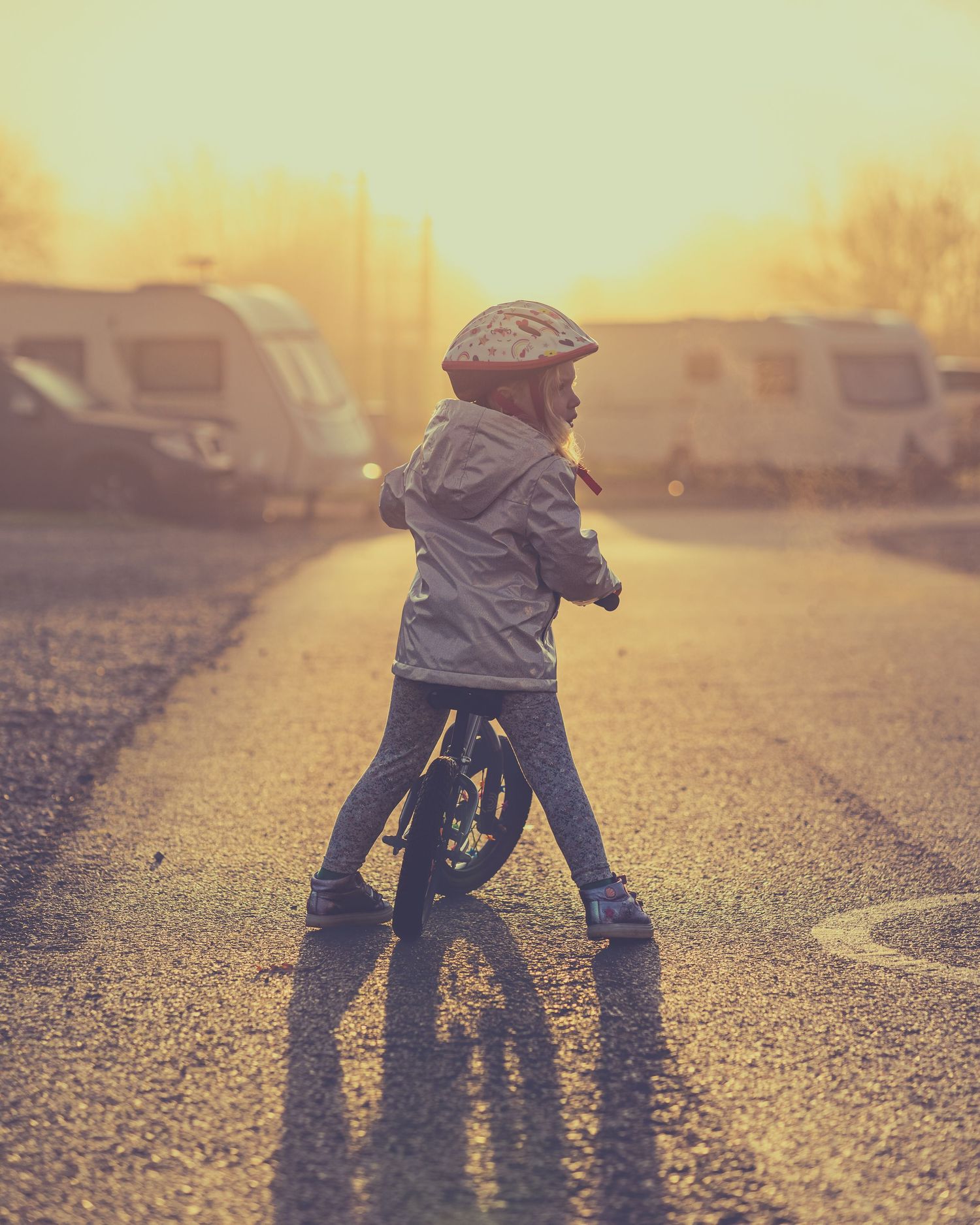 Child learning to ride bike at sunset with golden light creating silhouettes.