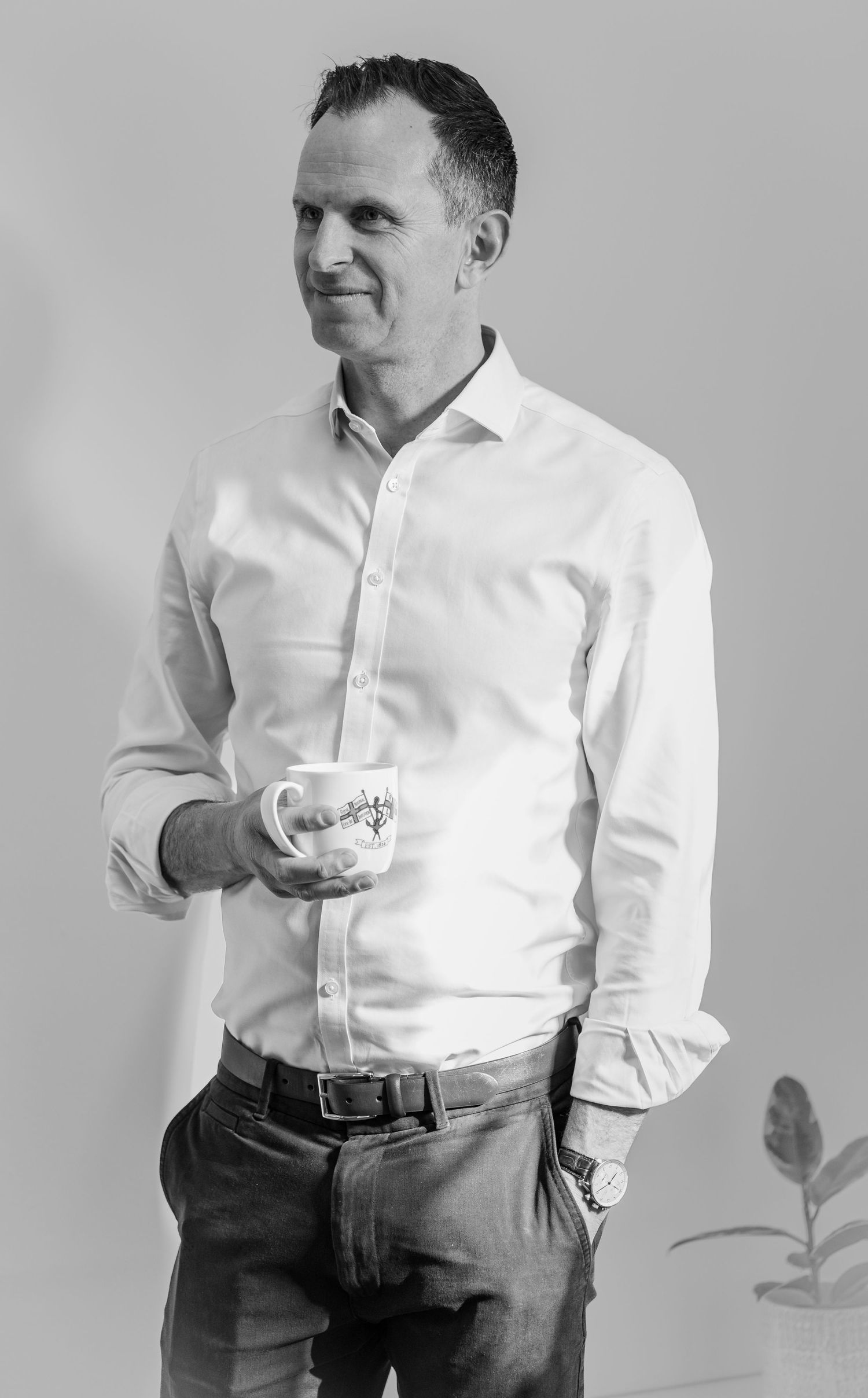 Professional portrait of person in white button-down shirt holding coffee cup against gray background.