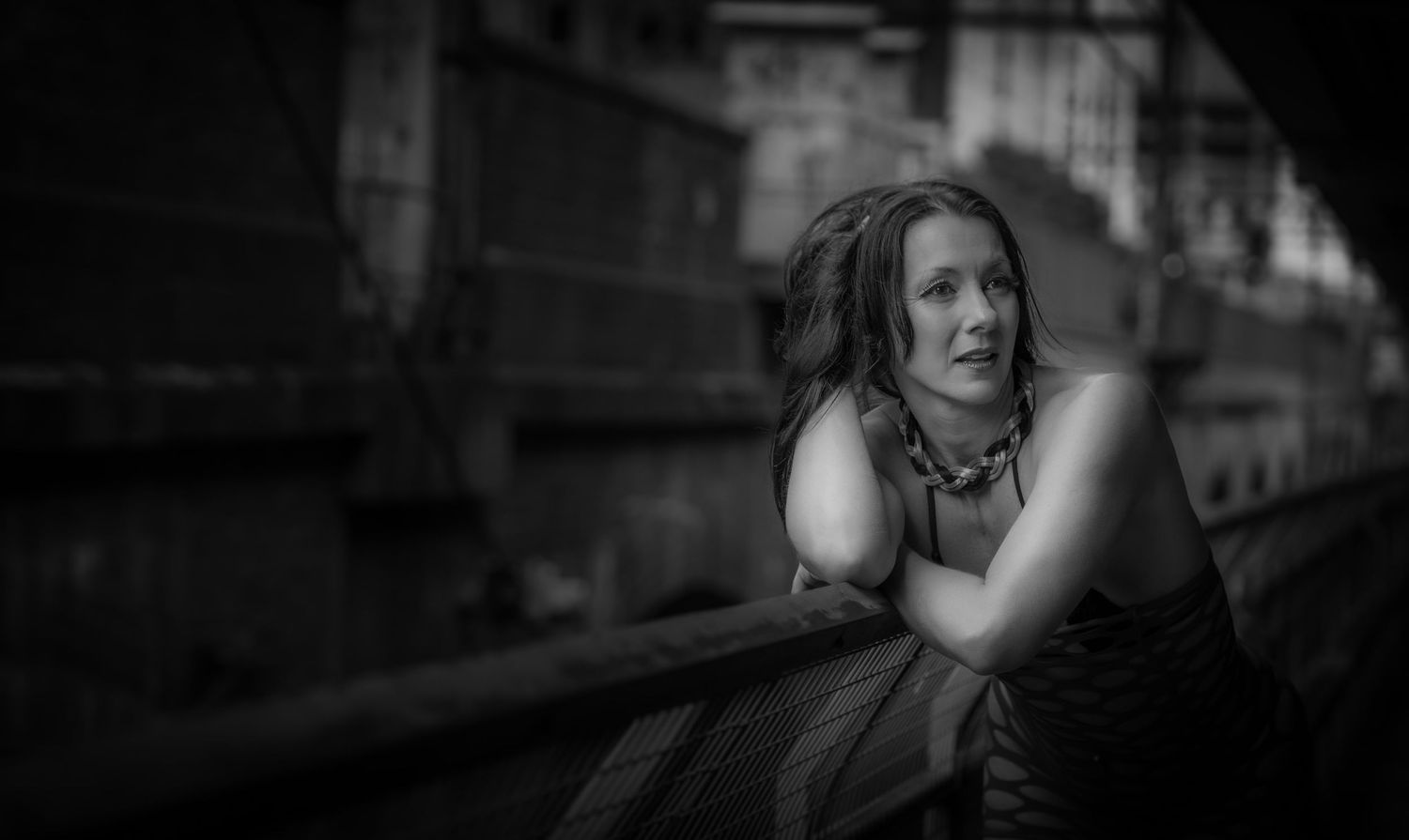 Moody black and white portrait of someone looking pensive while leaning on railing.