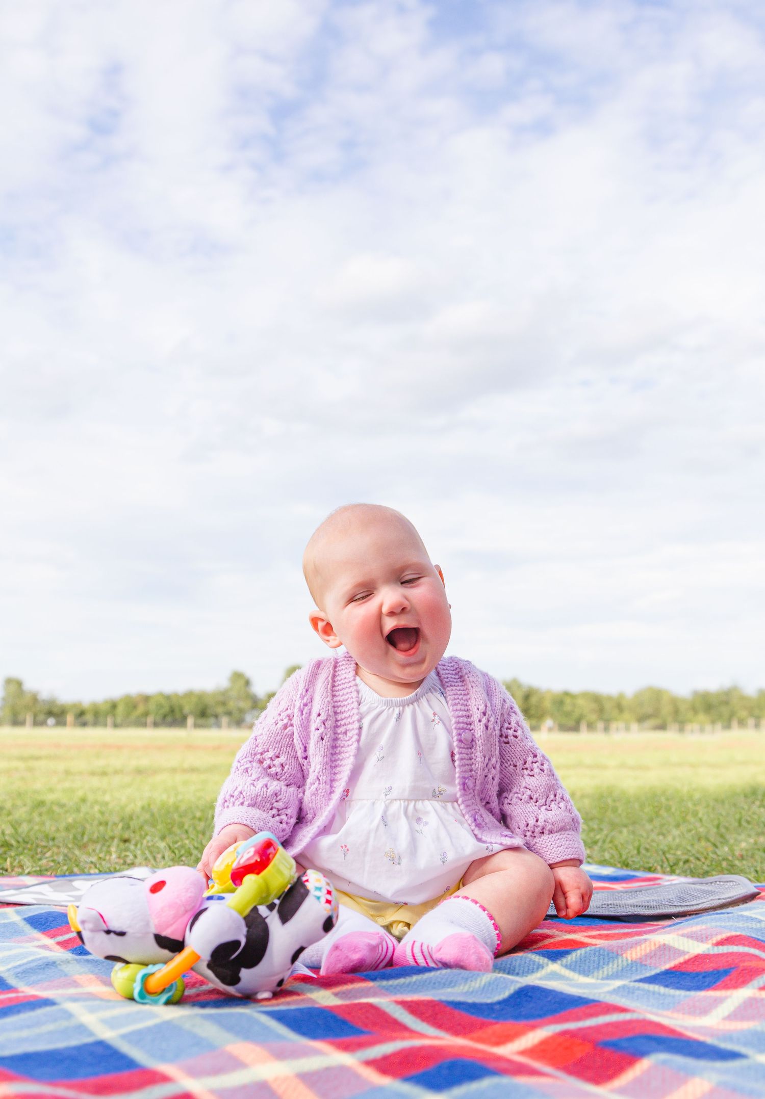 Baby in pink outfit sitting on colorful blanket during outdoor photoshoot.