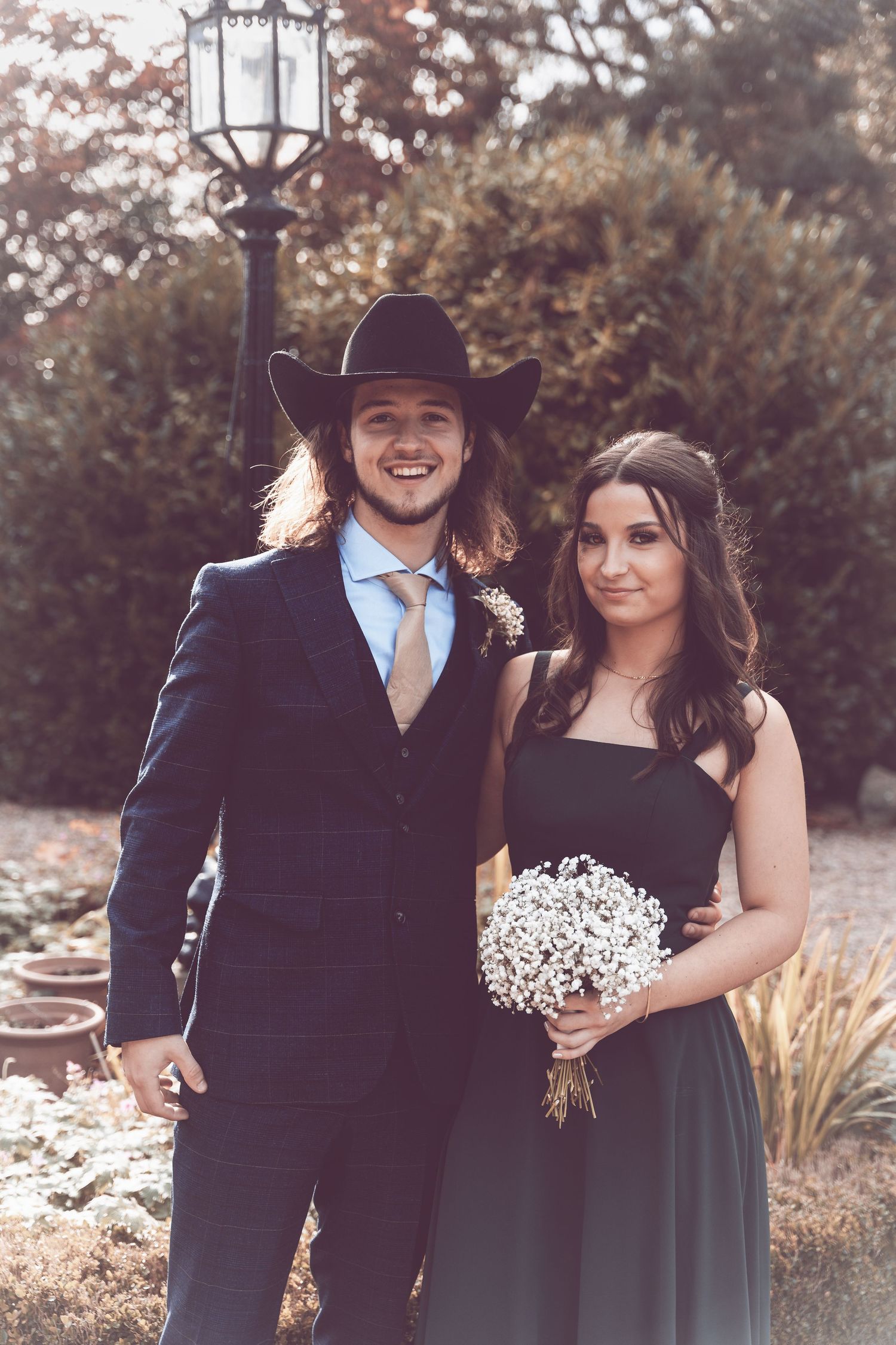 Couple in formal attire posing together outdoors with baby's breath bouquet.