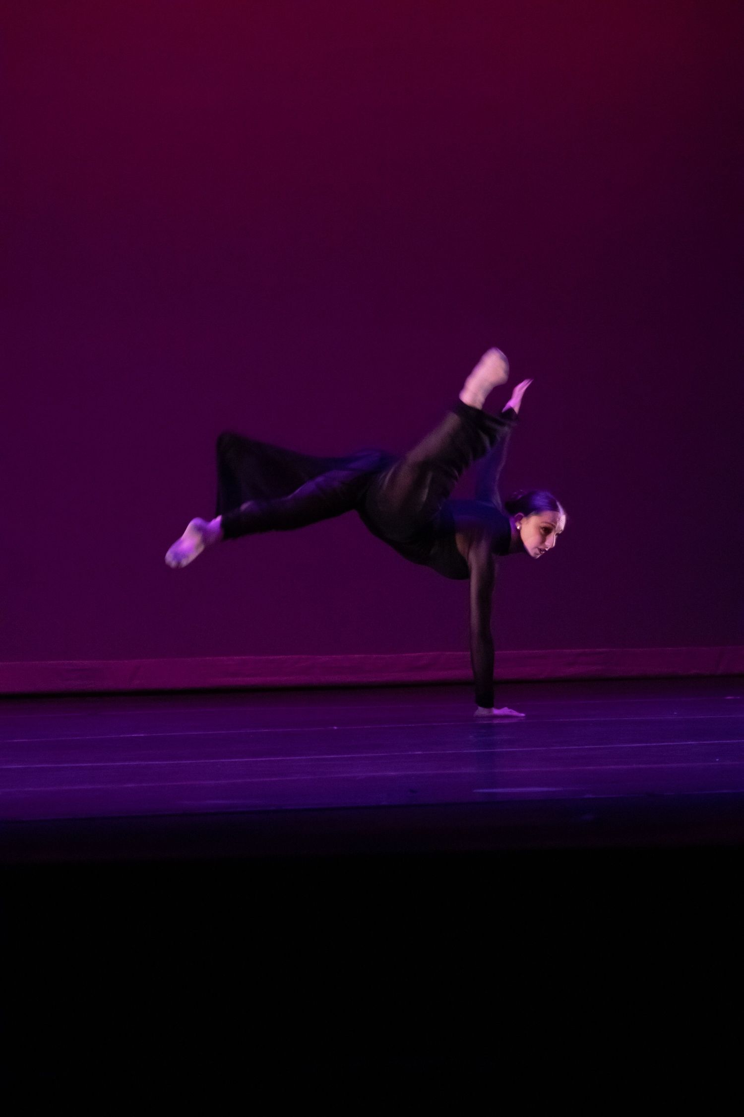 Dancer in black executes a one-handed balance with legs extended on purple stage.