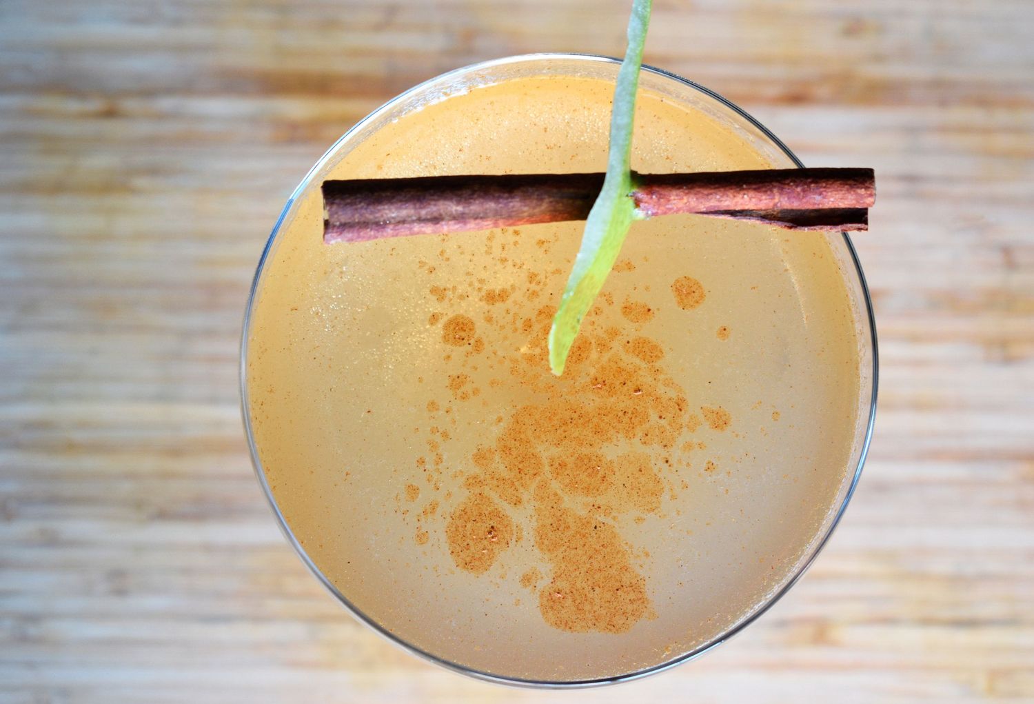 A frothy cocktail garnished with a cinnamon stick and green straw, dusted with orange spice powder.