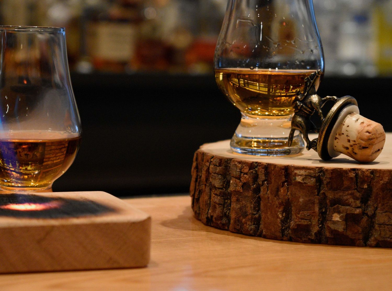Two Glencairn whisky glasses with a decorative cork stopper on a rustic wood slice.
