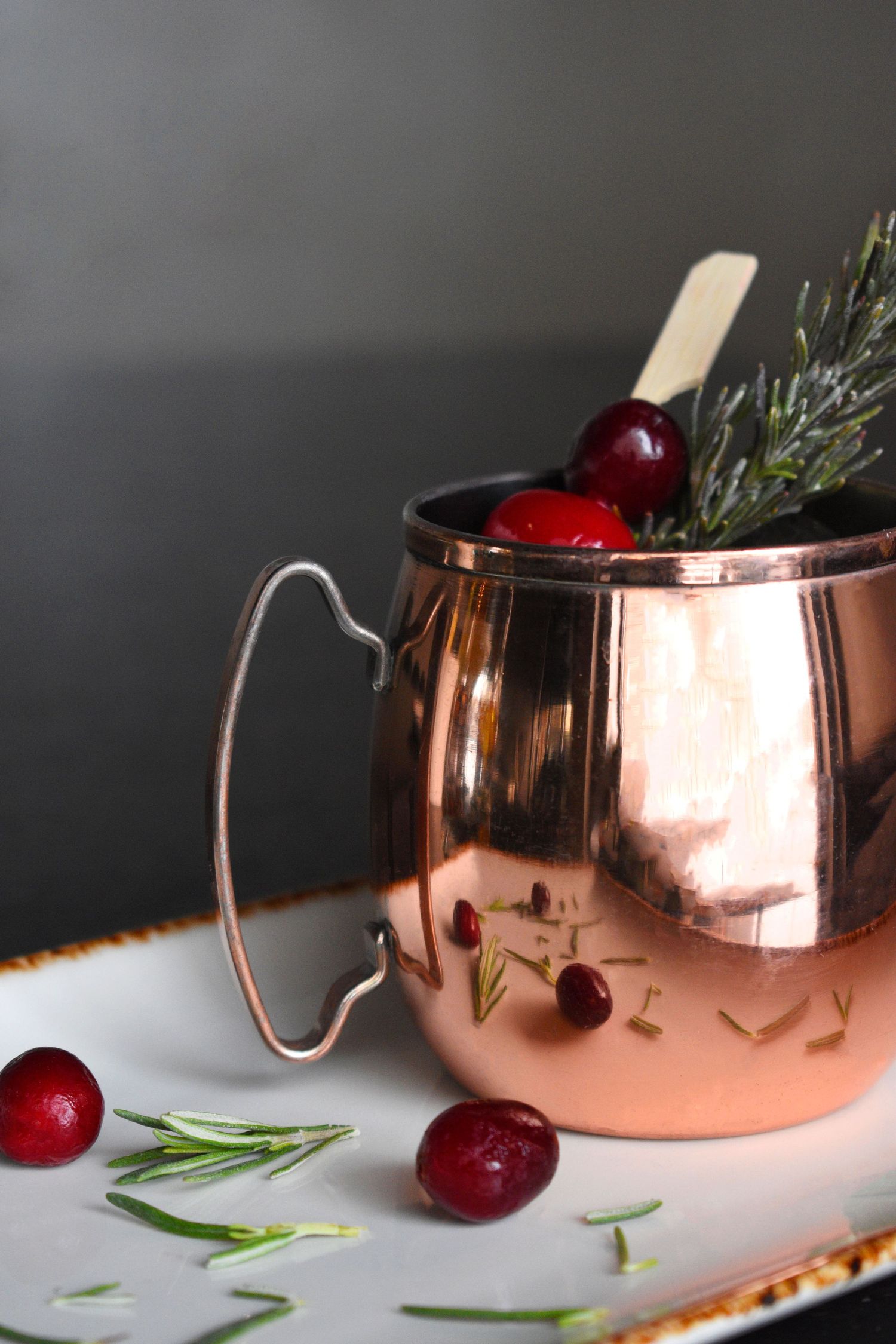 Cranberry Moscow Mule cocktail in a copper mug with rosemary and fresh cranberries.