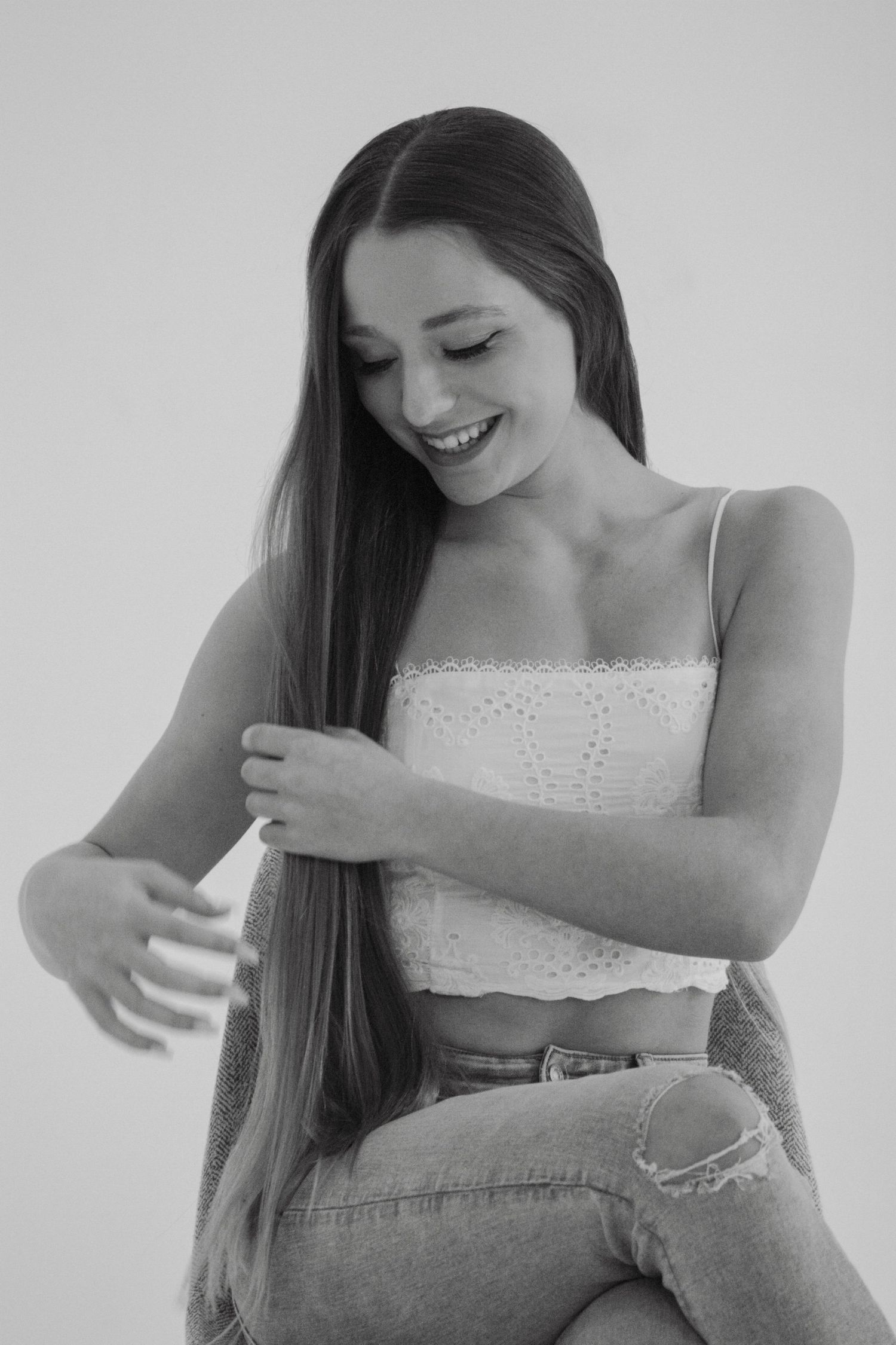 Smiling young woman with long hair in white crop top and jeans poses in black and white photo.