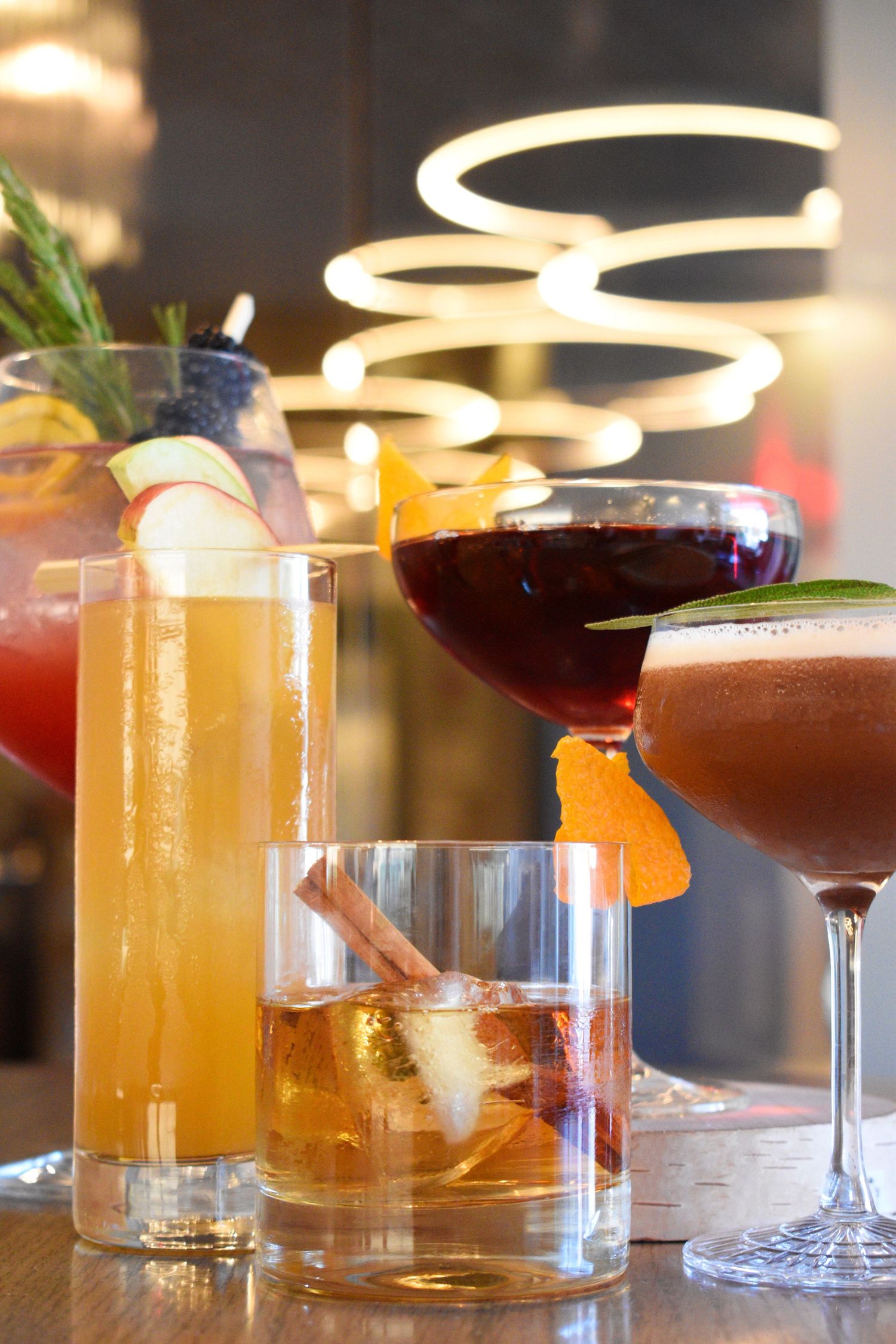 Assorted craft cocktails including highball, rocks glass, wine glass and coupe displayed on a bar counter.