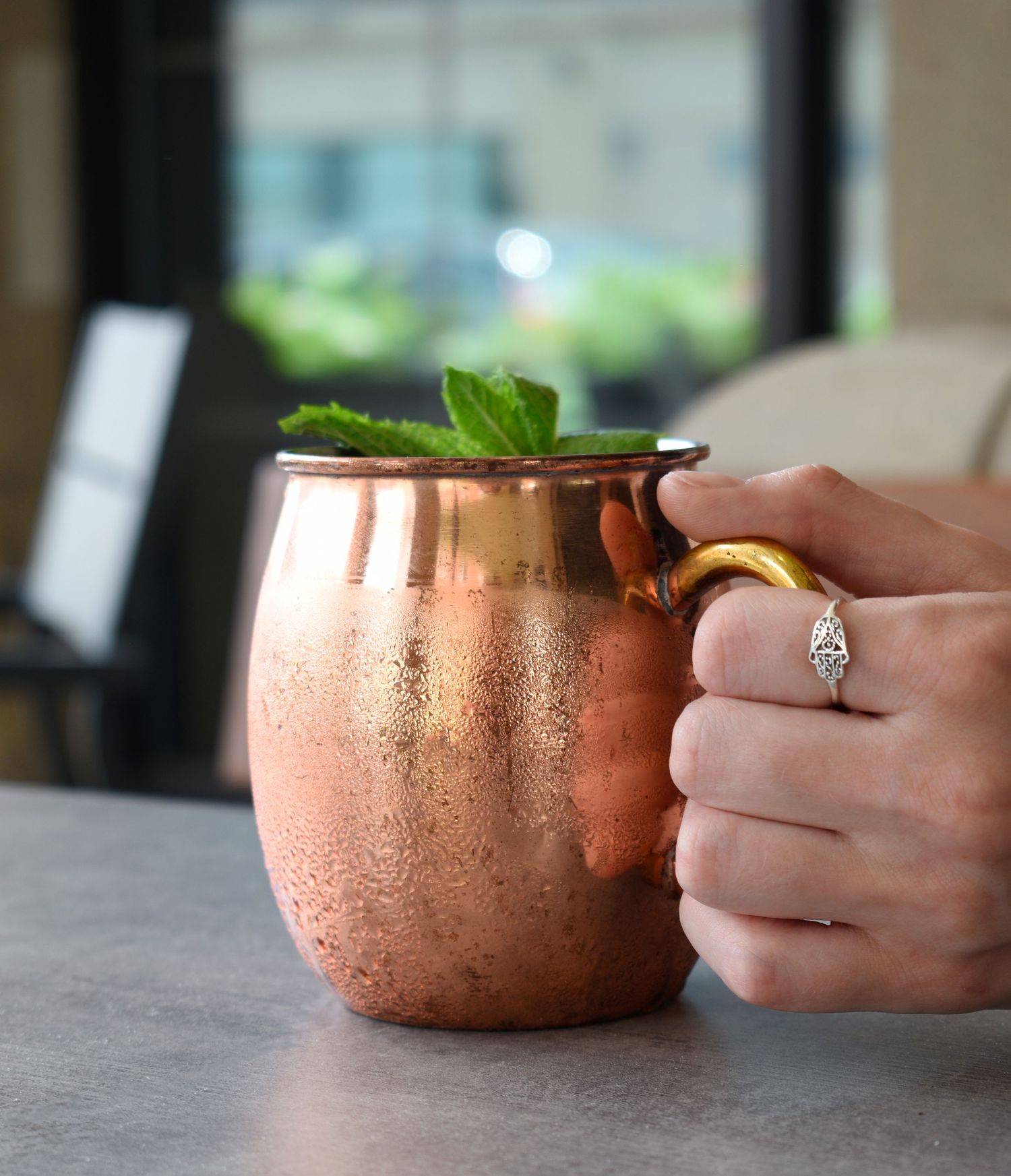 A copper Moscow Mule mug garnished with fresh mint leaves, held by a hand wearing a diamond ring.