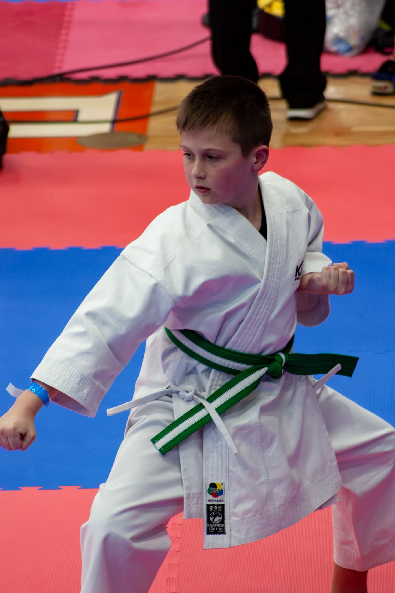 Young boy in white karate gi with green belt performs a martial arts kata at a karate competition.