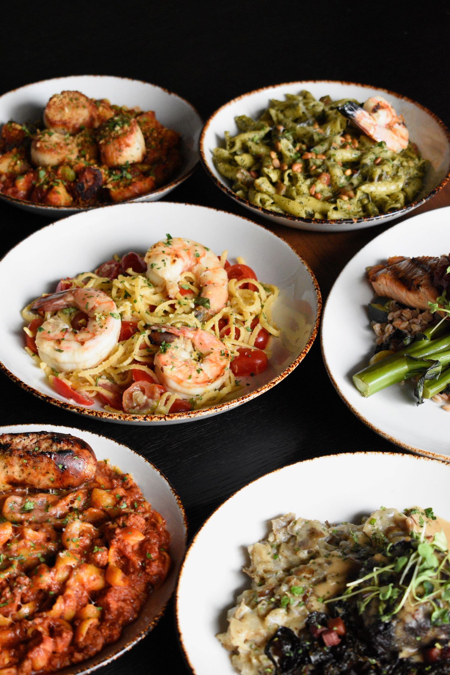 Assortment of six restaurant dishes including shrimp pasta, risotto, and seafood appetizers.