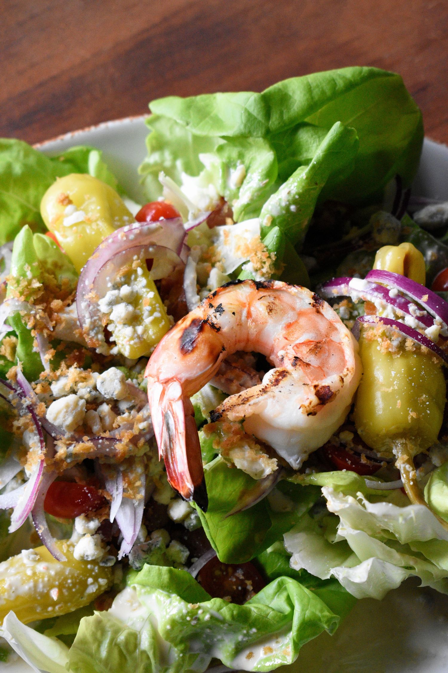 Close-up of a shrimp salad with grilled prawns, red onion, feta, greens, and golden peppers.