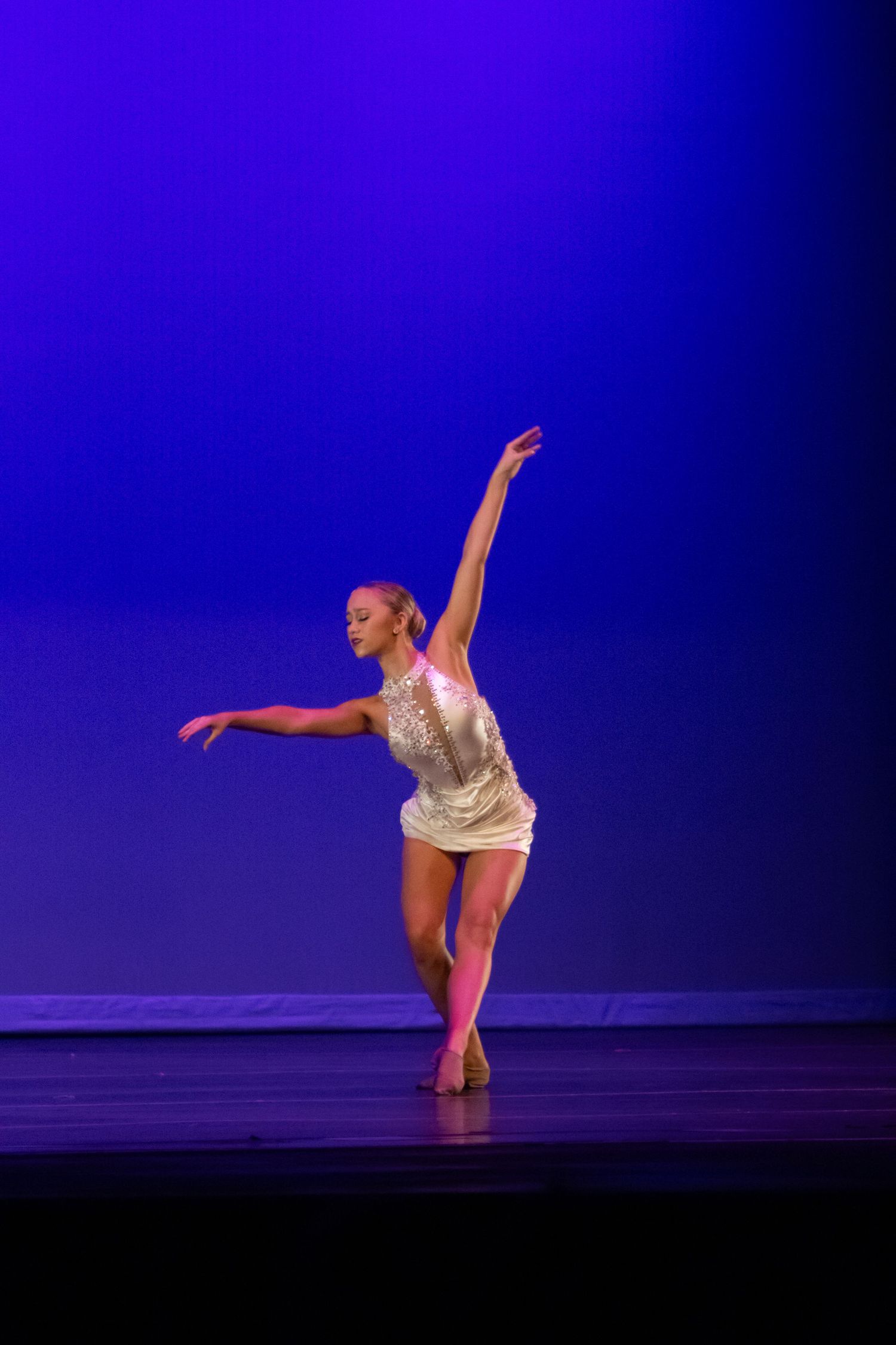 A female dancer in a gold sequined dress performs a contemporary routine on a blue-lit stage.
