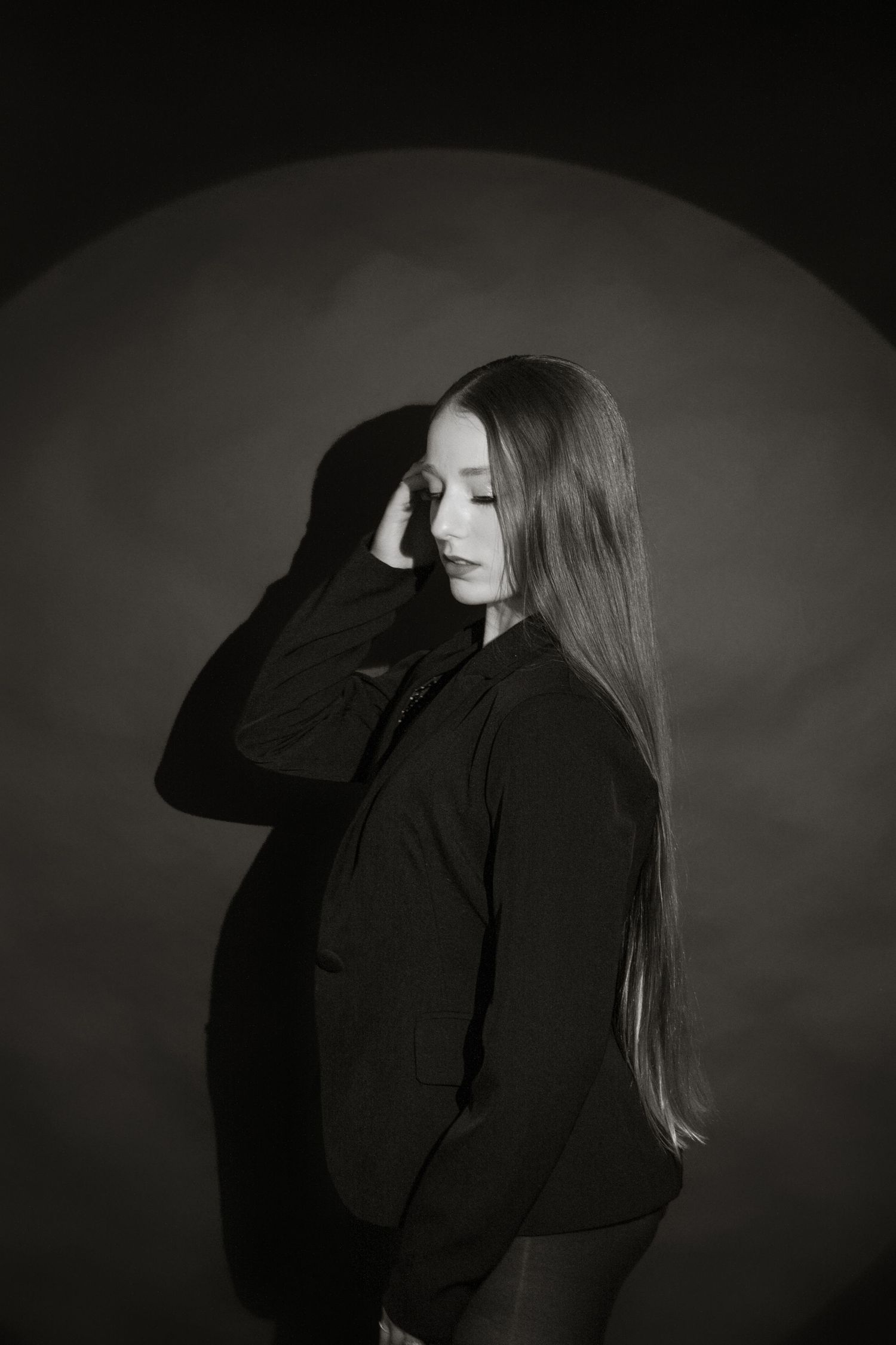 Young woman in black blazer poses with hand raised in moody black and white studio photo.