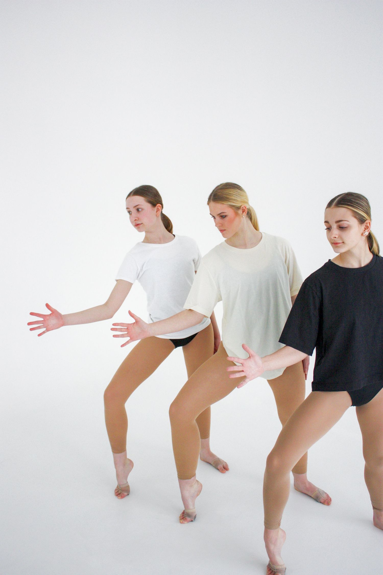 Three young female dancers in oversized t-shirts perform a synchronized contemporary dance routine on a white background.