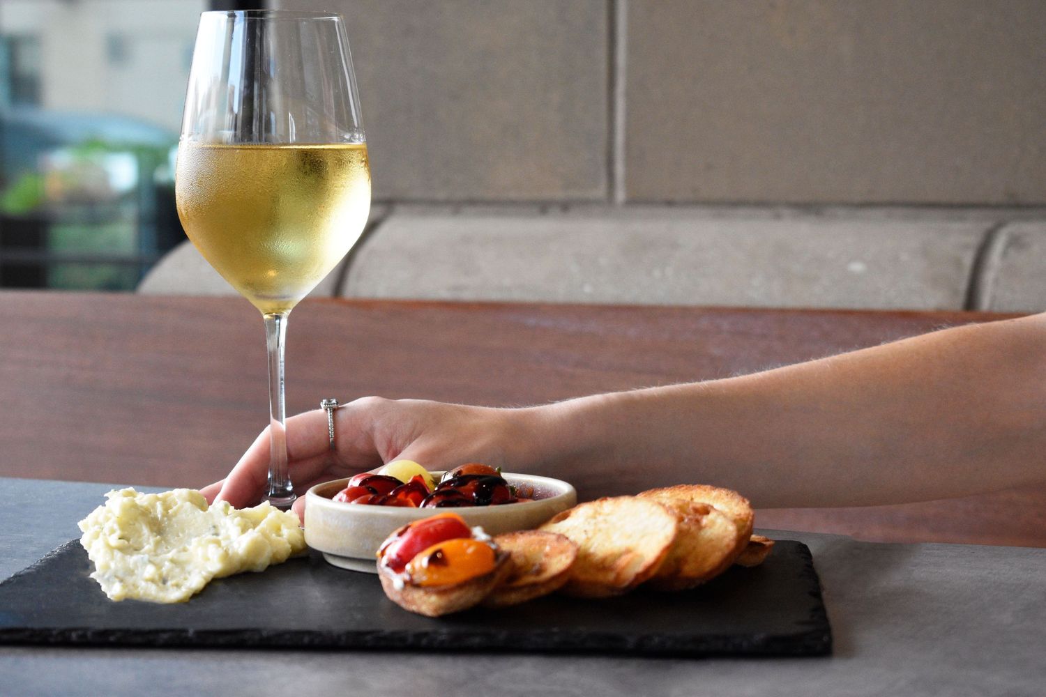 Hand reaching for wine glass beside slate charcuterie board with cheese, peppers, and crostini. Food & beverage photography in Tampa, FL.