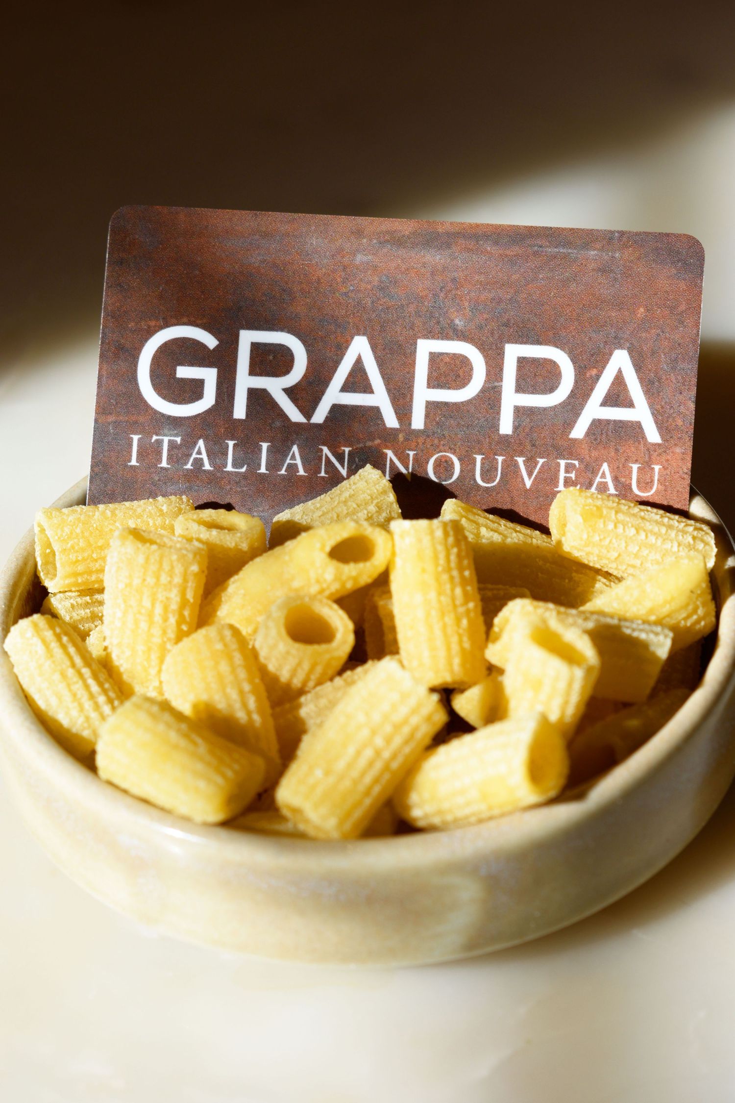 Bowl of uncooked rigatoni pasta with Grappa Italian Nouveau restaurant card.