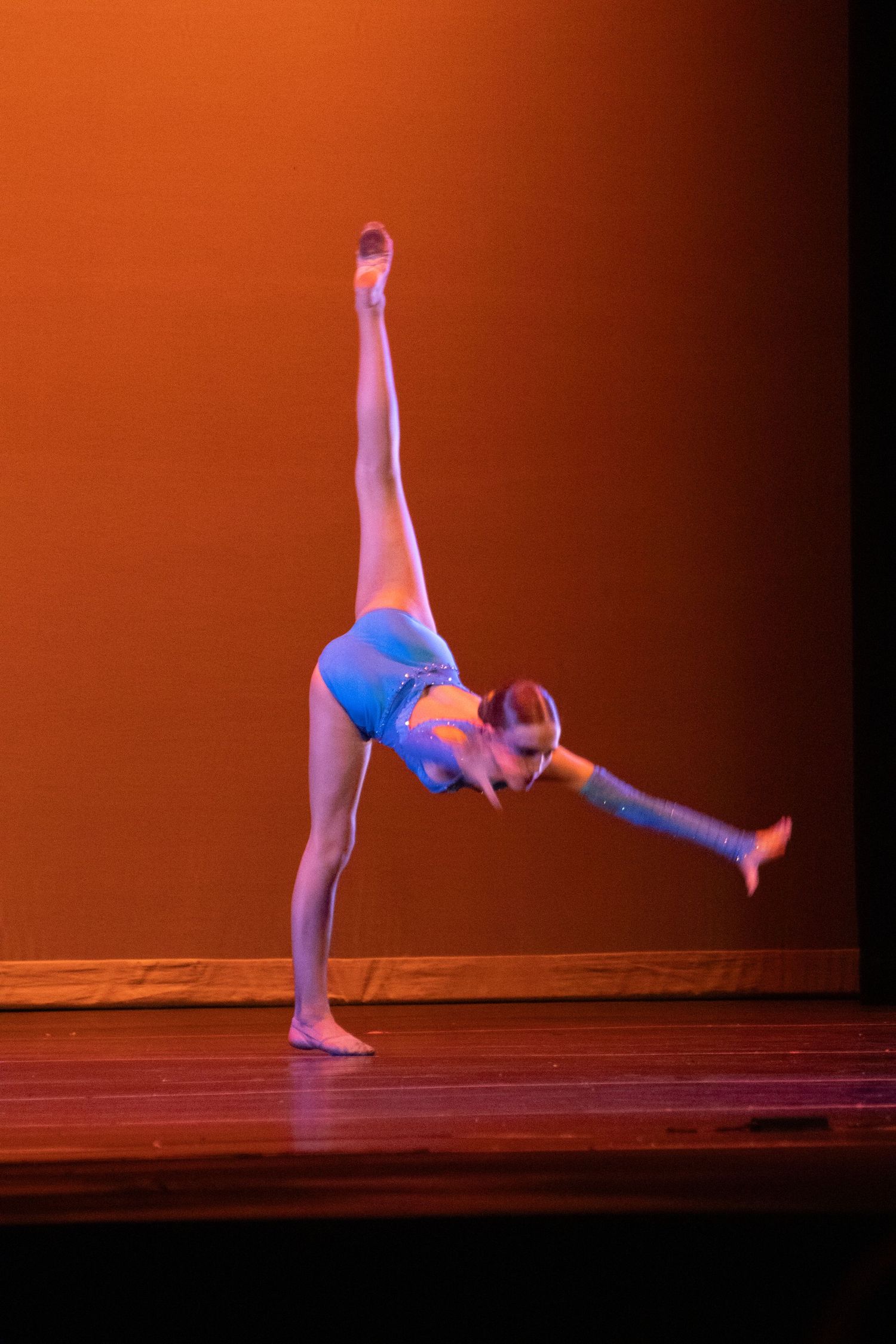 Young gymnast performs a one-handed cartwheel on stage under warm orange lighting.